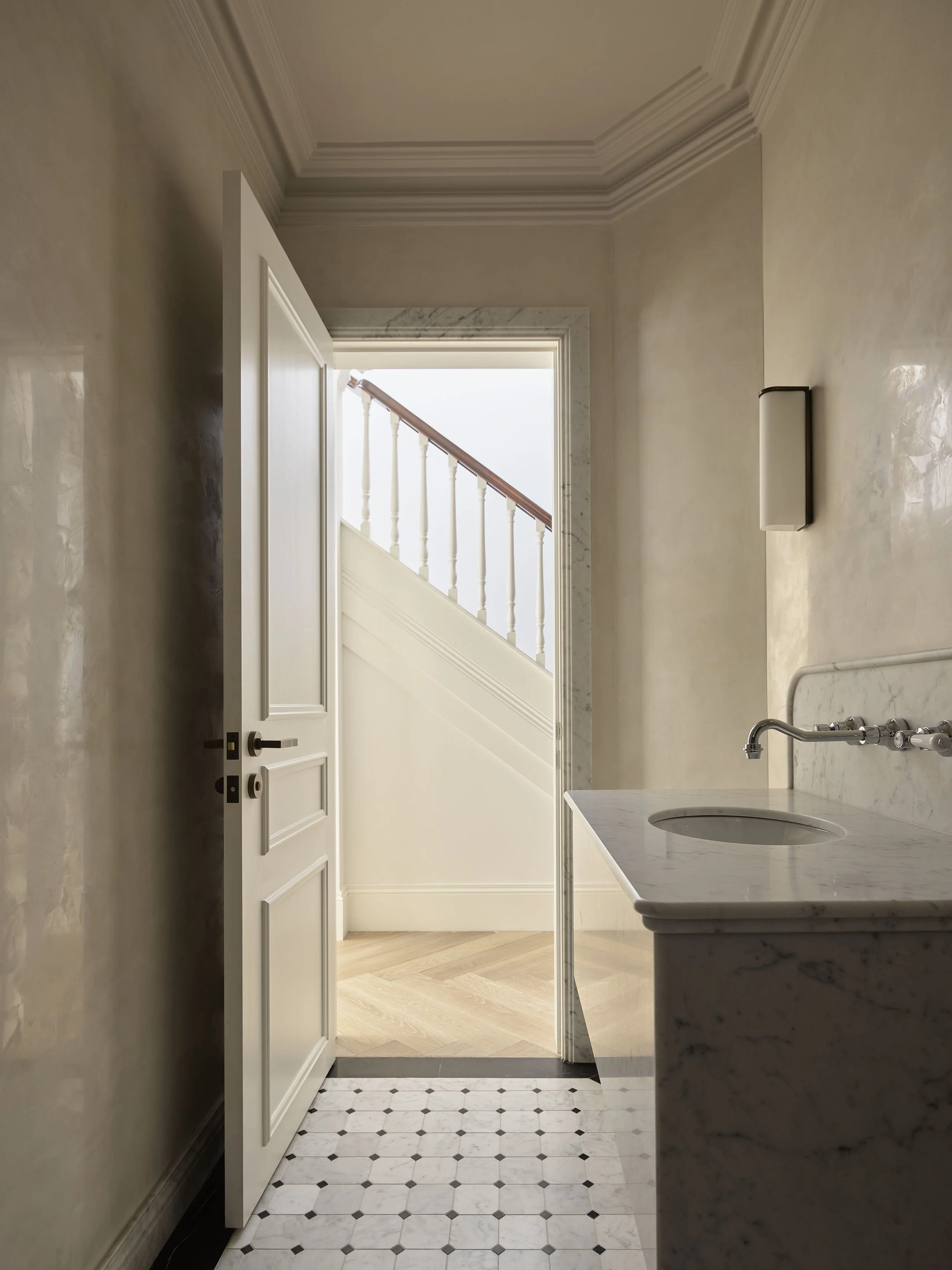 Interior view of a vintage-style corridor with an open door leading to a staircase, featuring marble floors and beige walls.