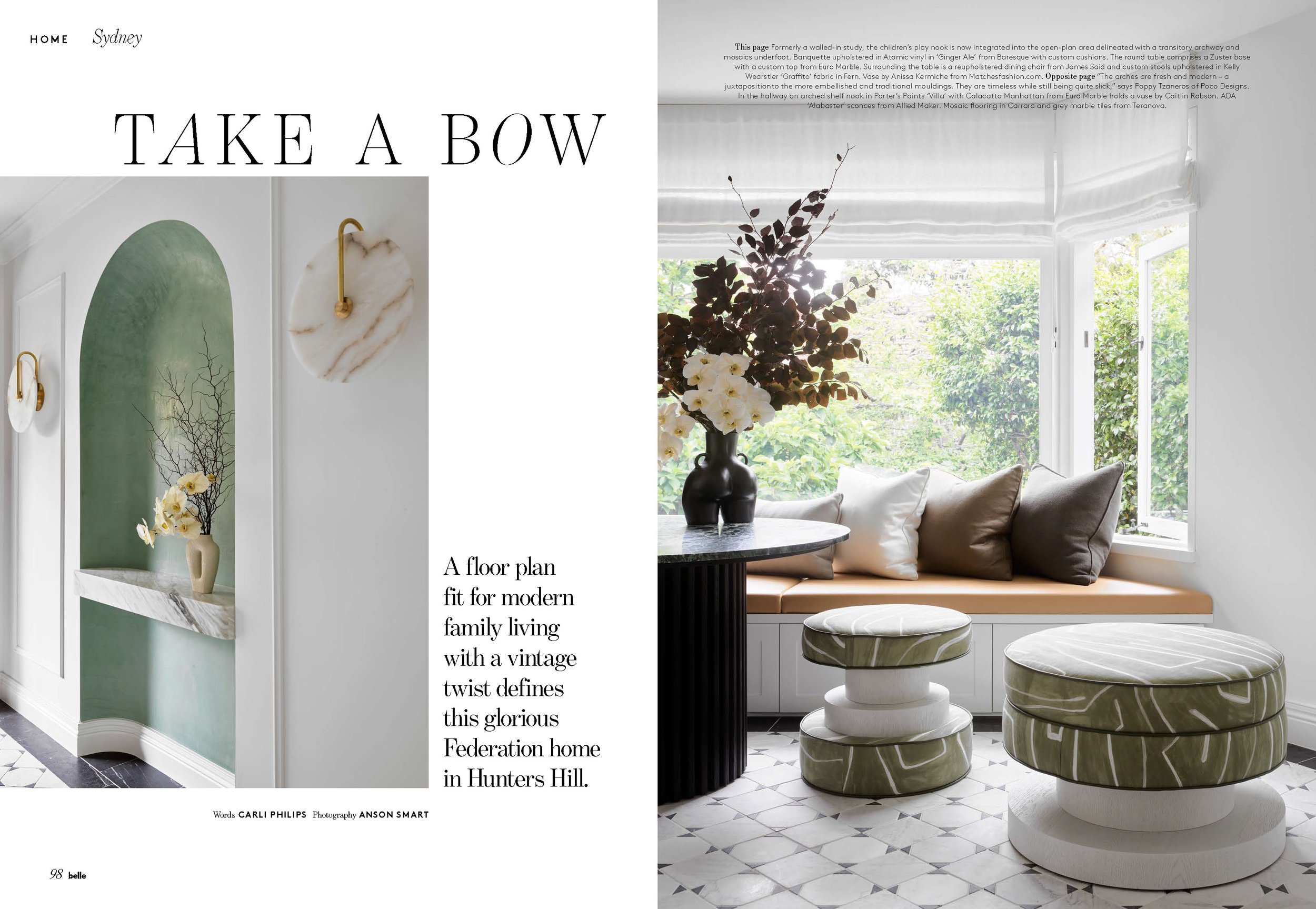 Interior of a modern living room with a window seat, decorated with cushions and a large vase of flowers, with natural light streaming in.