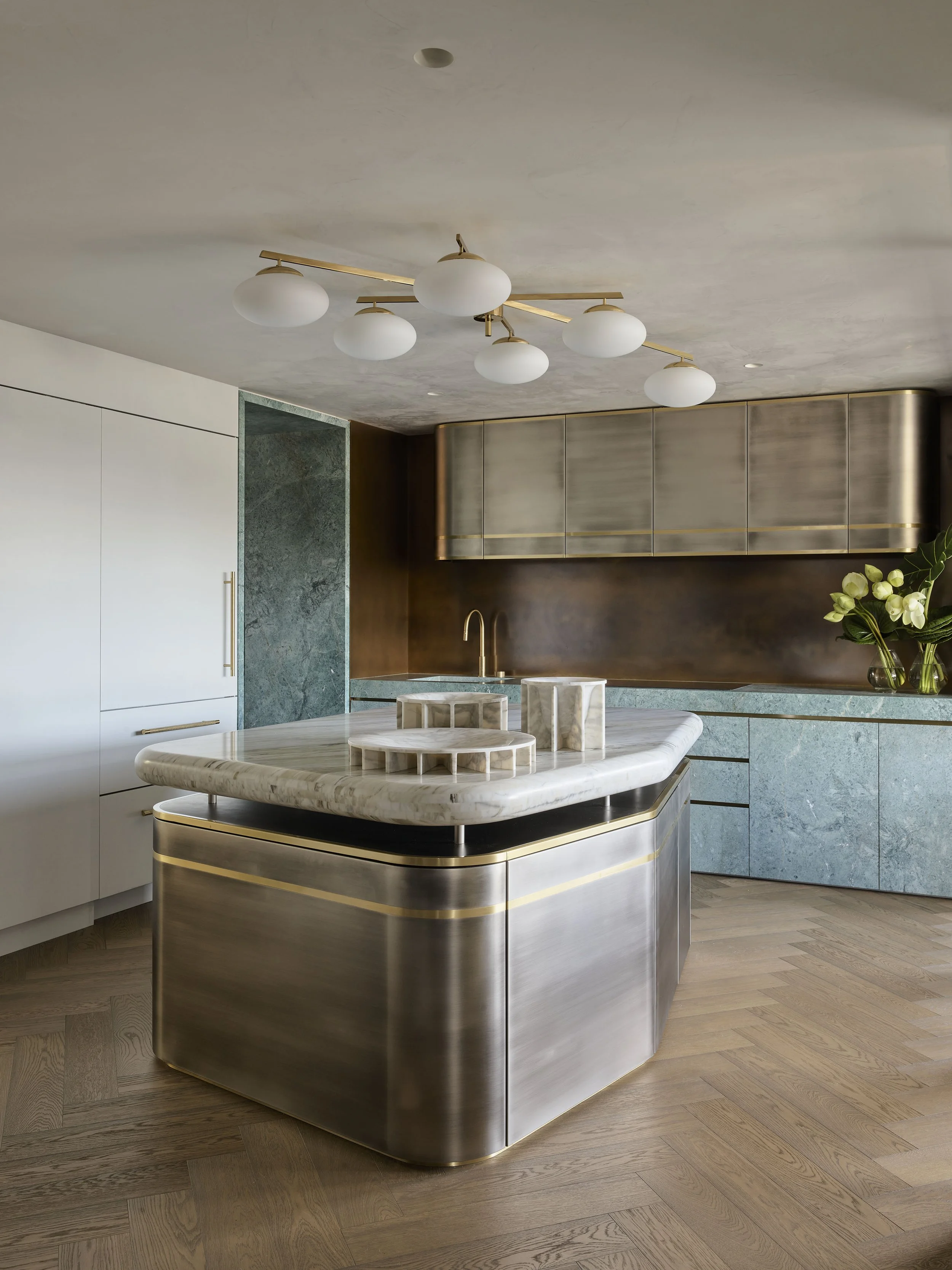 Modern kitchen with marble island, gold accents, and green marble walls.