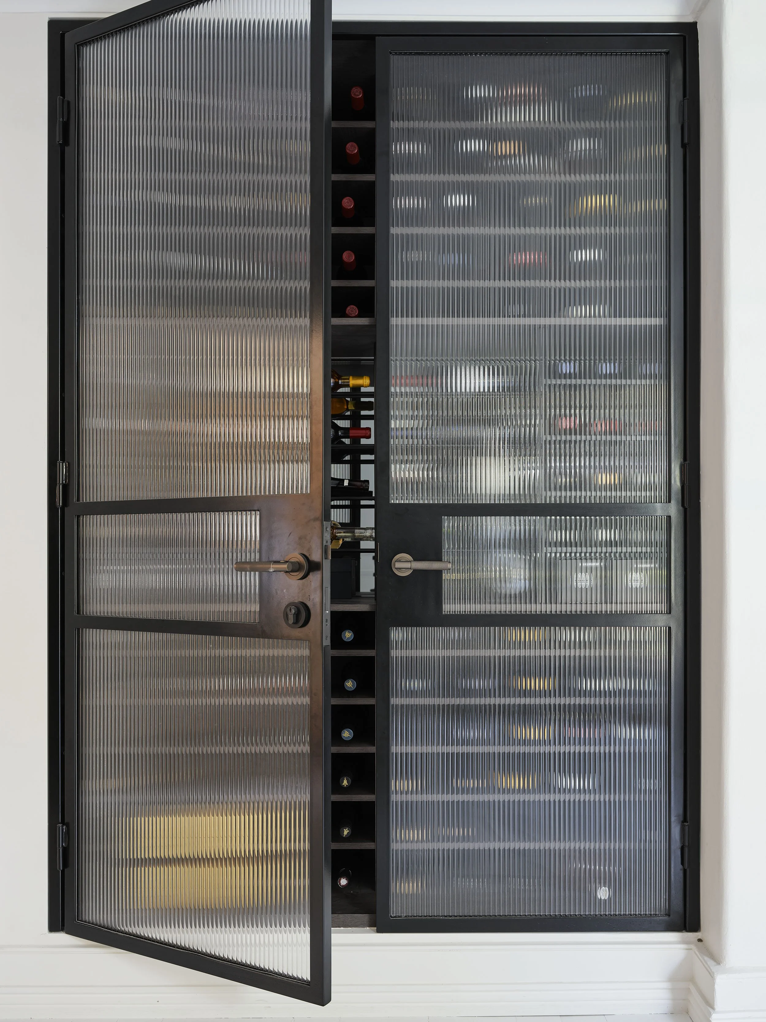A black wine cellar cabinet with glass-paneled doors, partially open, revealing wine bottles stored on shelves inside.