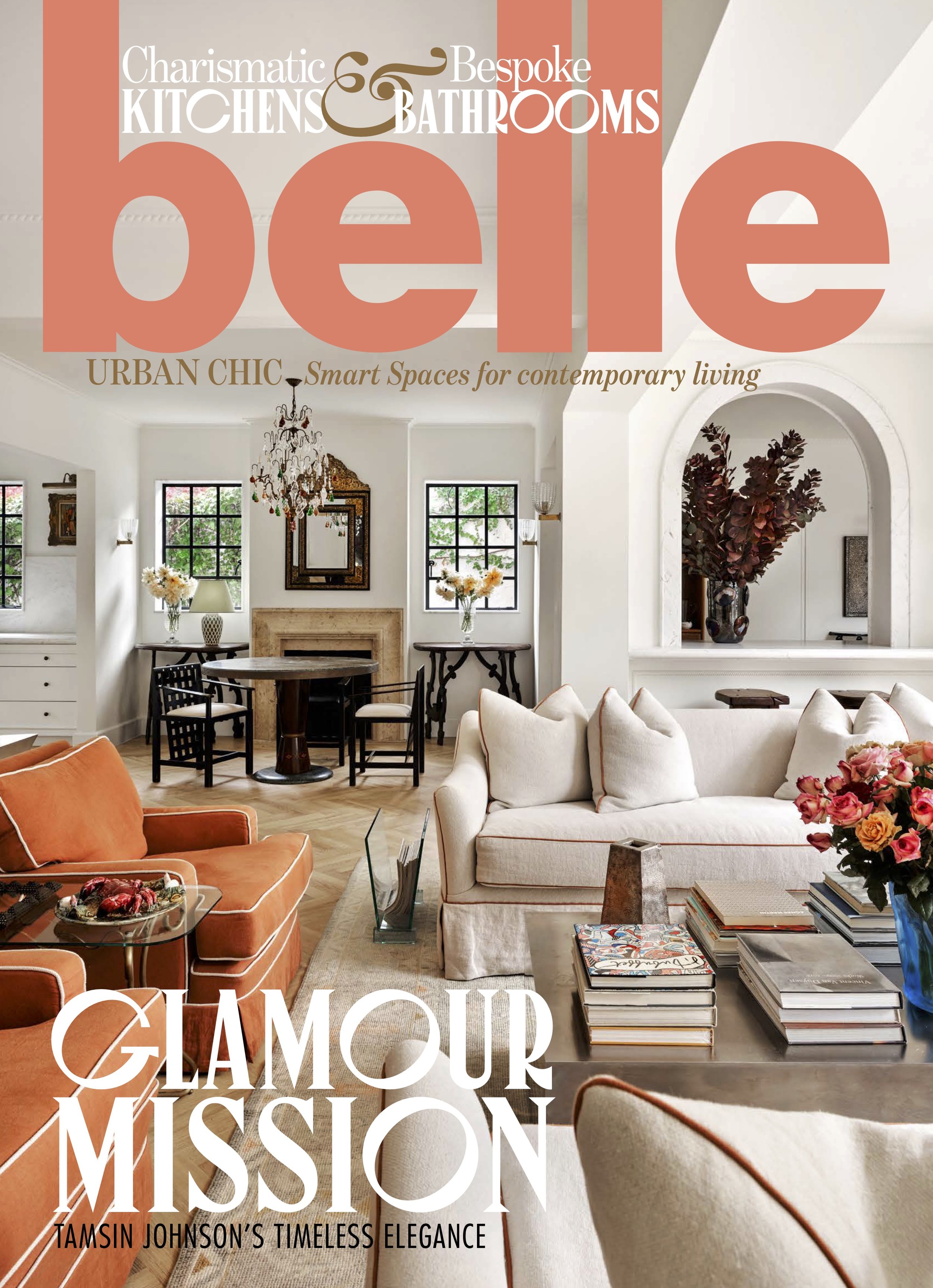 Cover of Belle magazine featuring an elegant living room with white walls, a chandelier, sofas, and a coffee table with stacked books and flowers.