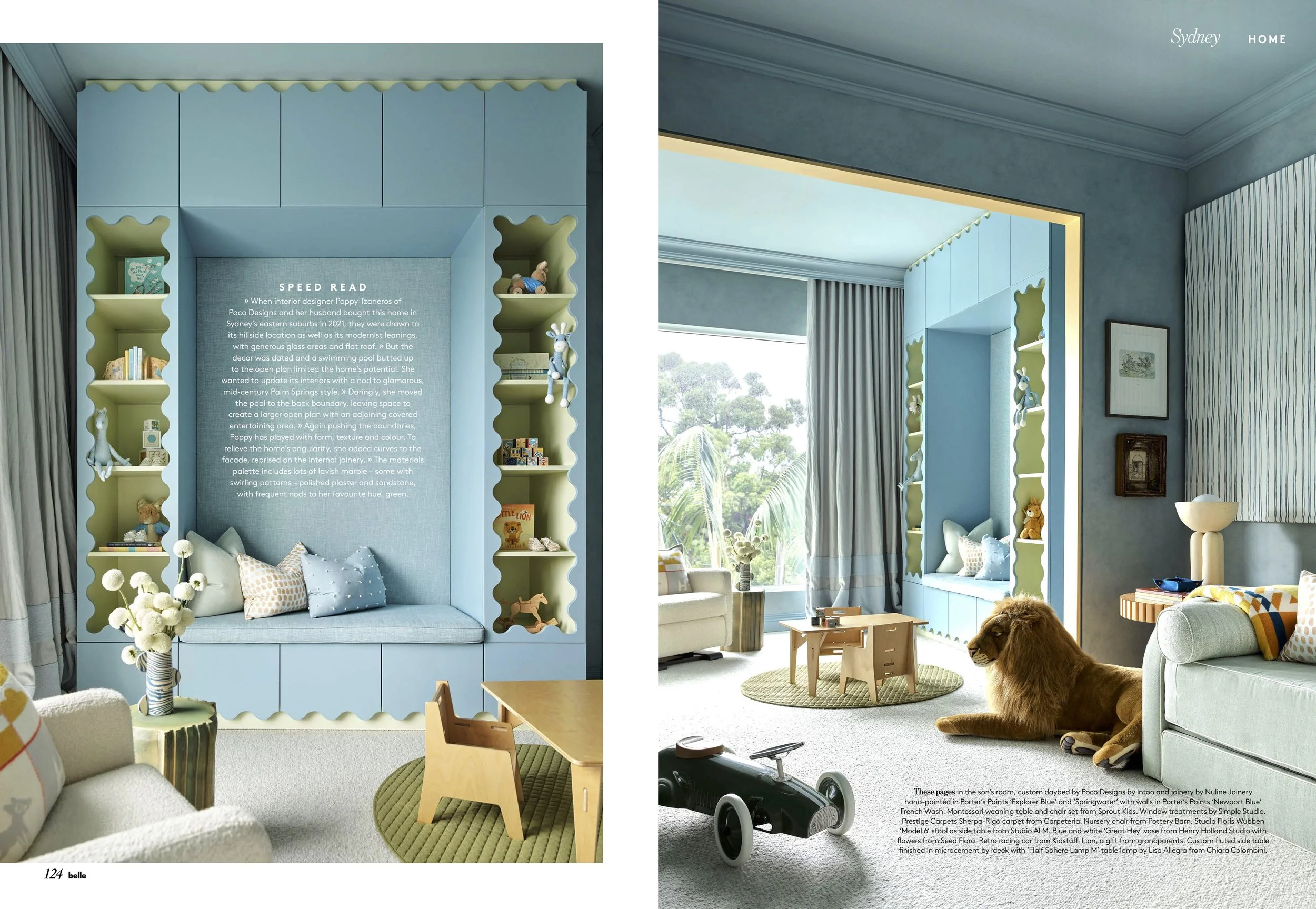 Living room with a built-in blue window seat with shelves filled with toys and books, a beige sofa, a coffee table, a lion plush toy, and a large window with curtains overlooking greenery.