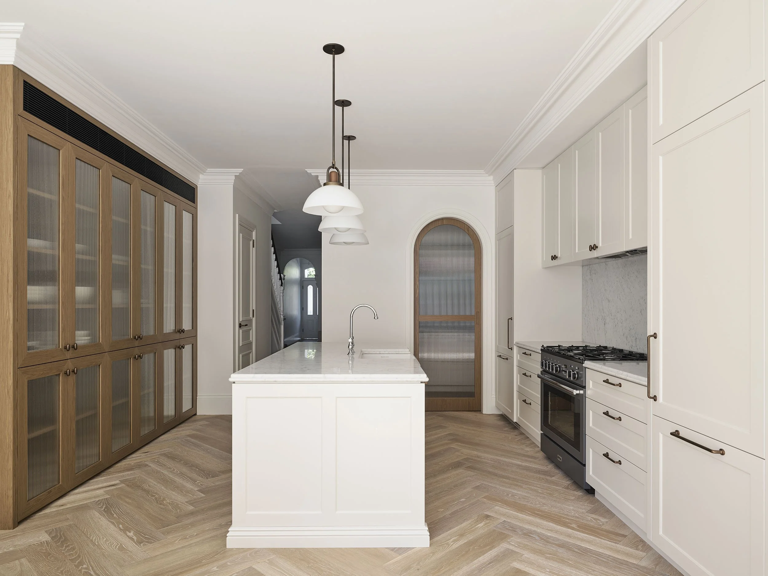 Modern kitchen with white cabinets, stainless steel stove, marble backsplash, and a large central island with a marble countertop. Features wooden accents on a large pantry and a door with wooden trim, light wood flooring, and hanging pendant lights.
