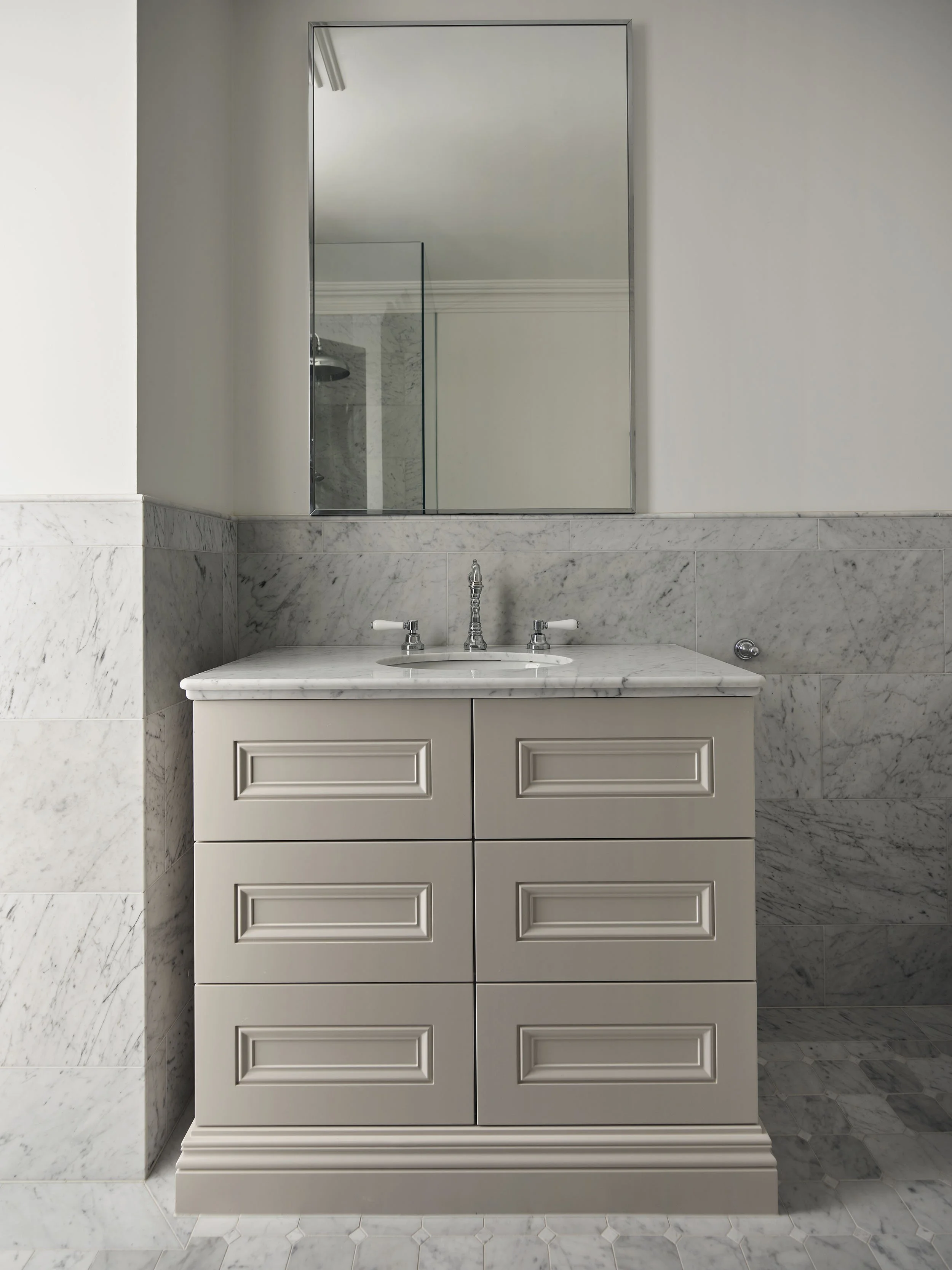 Bathroom vanity with a marble countertop, six drawers, a mirror above, and marble tile walls and floor.