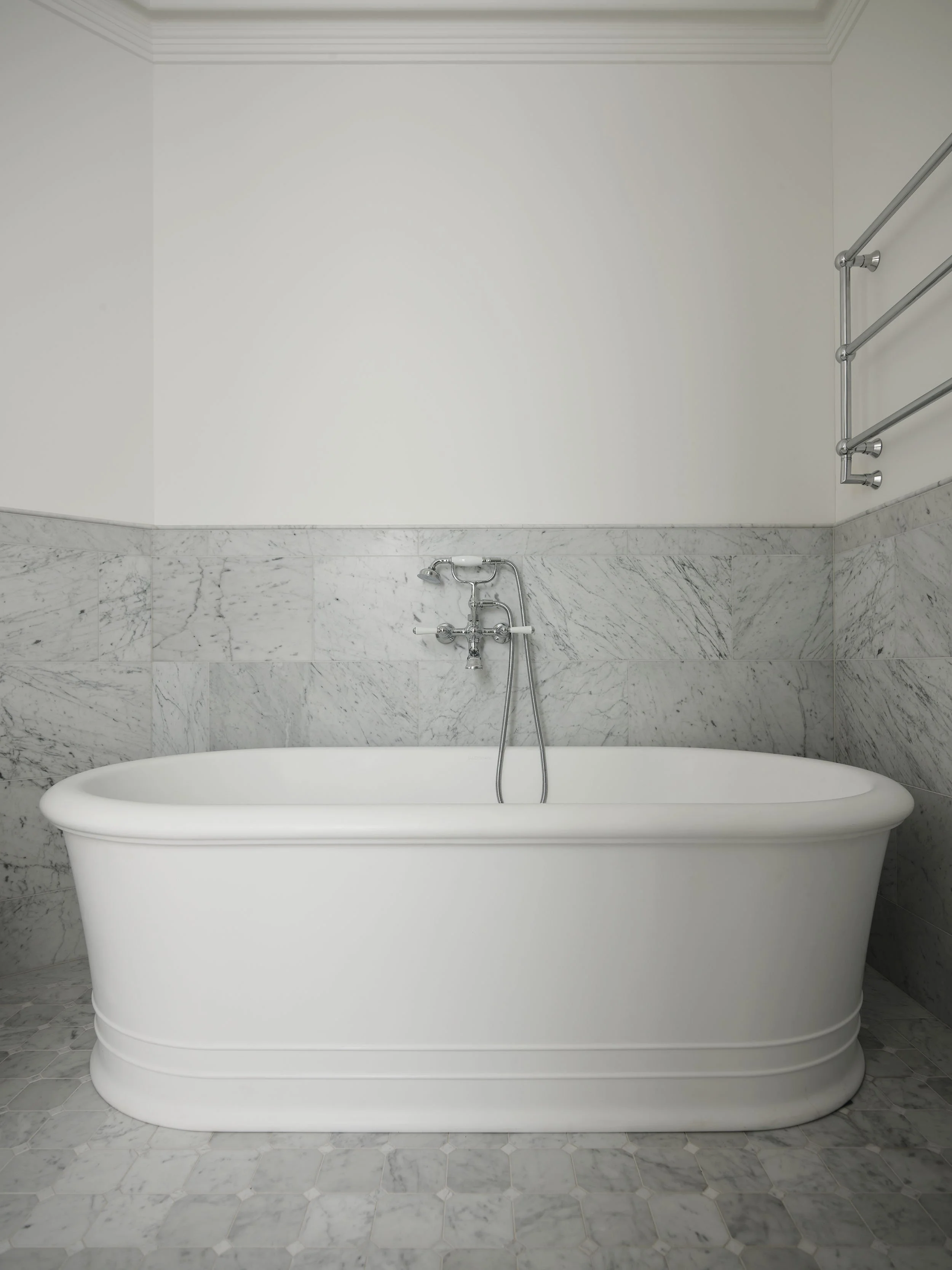 A white bathtub set against a marble tiled wall in a minimalist bathroom.