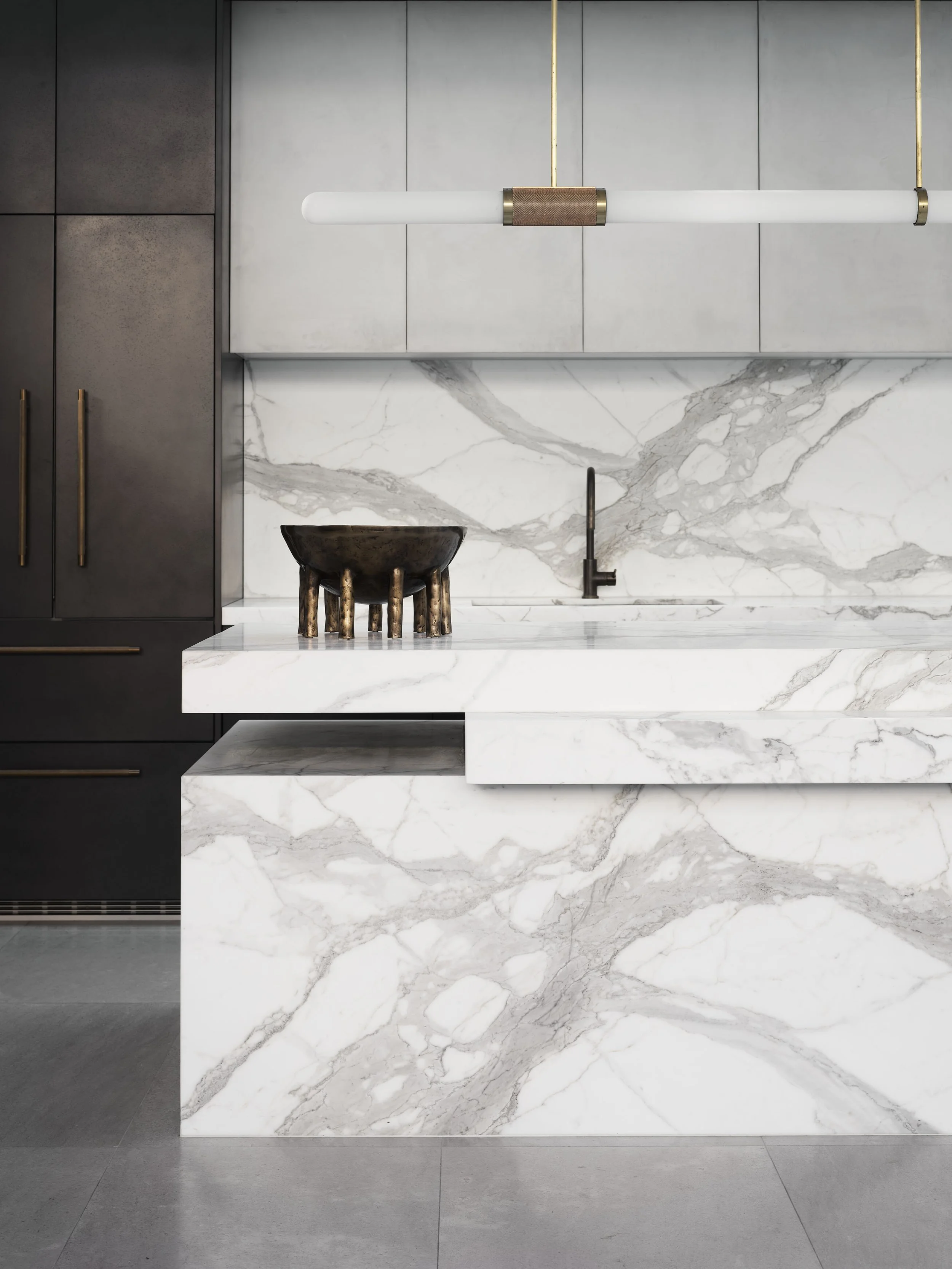 Modern kitchen with a marble island, dark cabinetry, and gold accents, including a hanging light fixture.