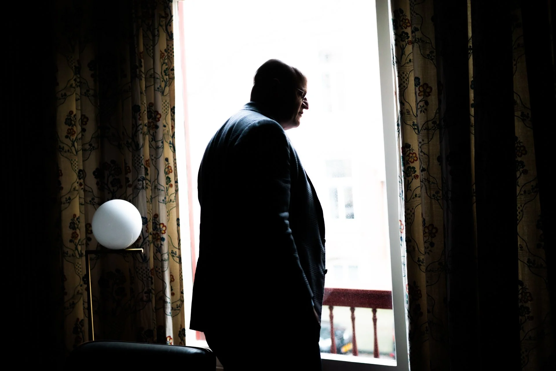 Silhouette of a man standing by a window with curtains, backlit by bright daylight.