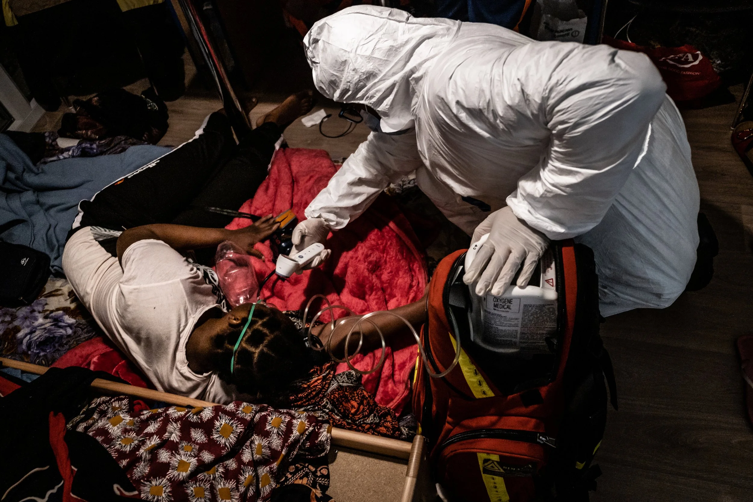 Emergency medical personnel providing medical assistance to a woman lying on a bed in a dimly lit room.
