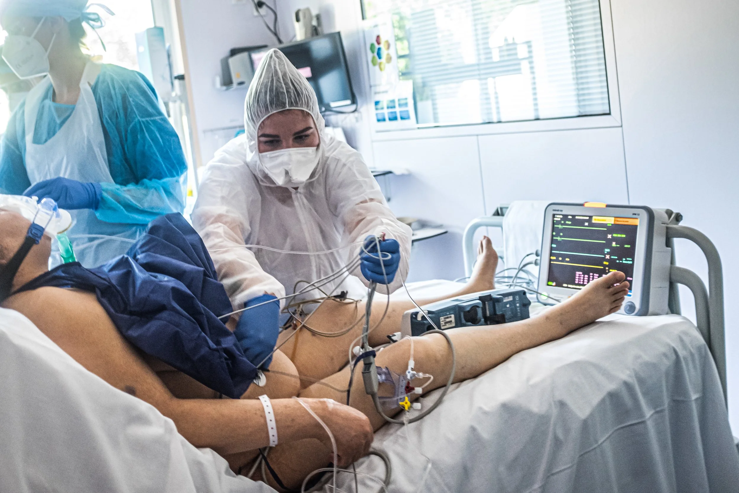 Medical professionals attending to a patient on a hospital bed in an intensive care unit, with monitoring equipment and medical devices.