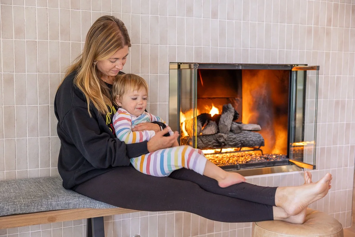 Mom holding toddler on bench by fireplace, Lake Tahoe cabin, documentary family photography