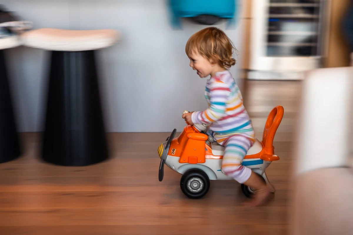 Toddler riding toy airplane on hardwood floor, Lake Tahoe cabin, documentary family photography
