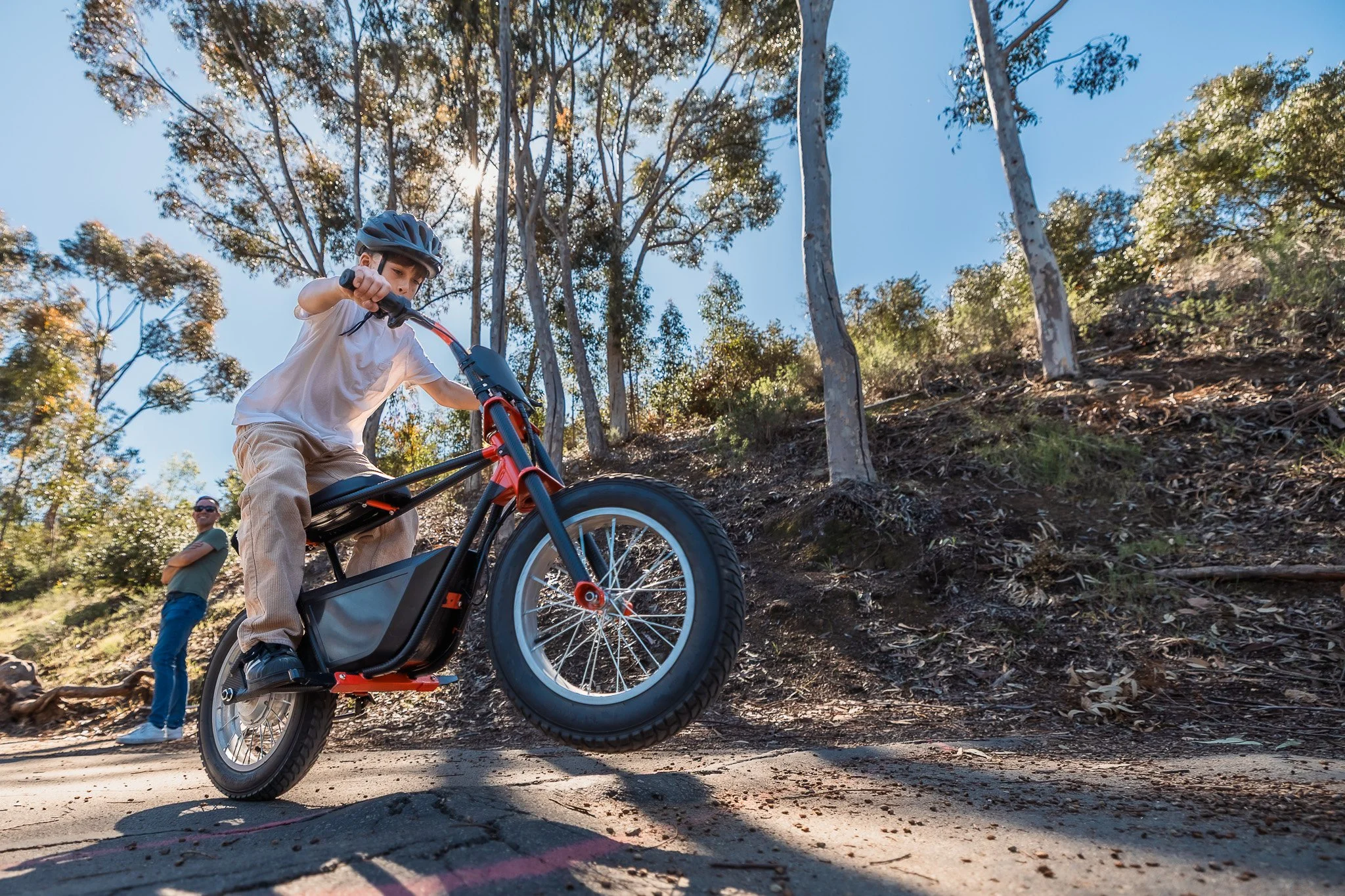 Boy riding electric dirt bike on outdoor trail with dad watching, documentary family photography San Diego