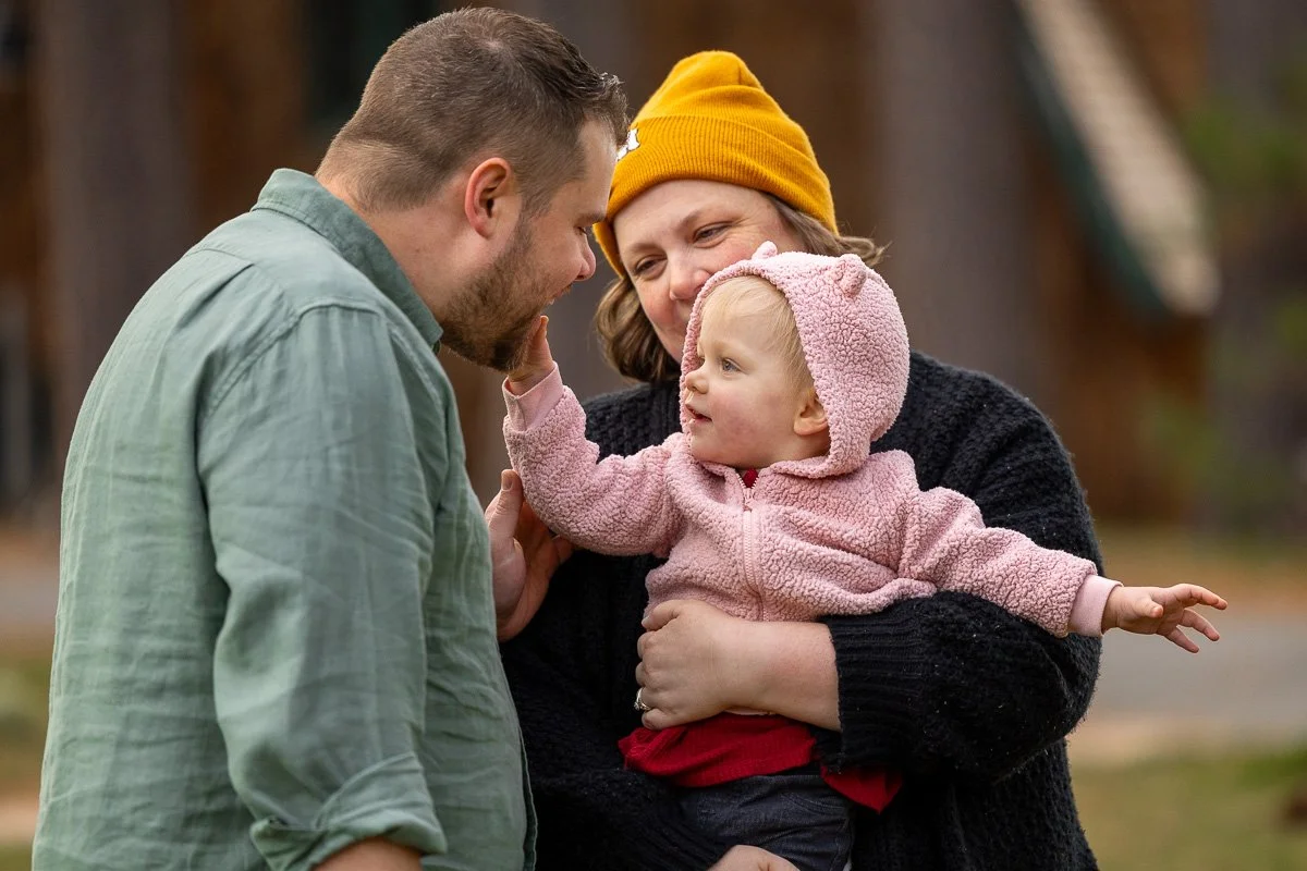 Mother holding her toddler who reaches out to touch dad's face during a documentary family photography session at Camp Richardson, Lake Tahoe