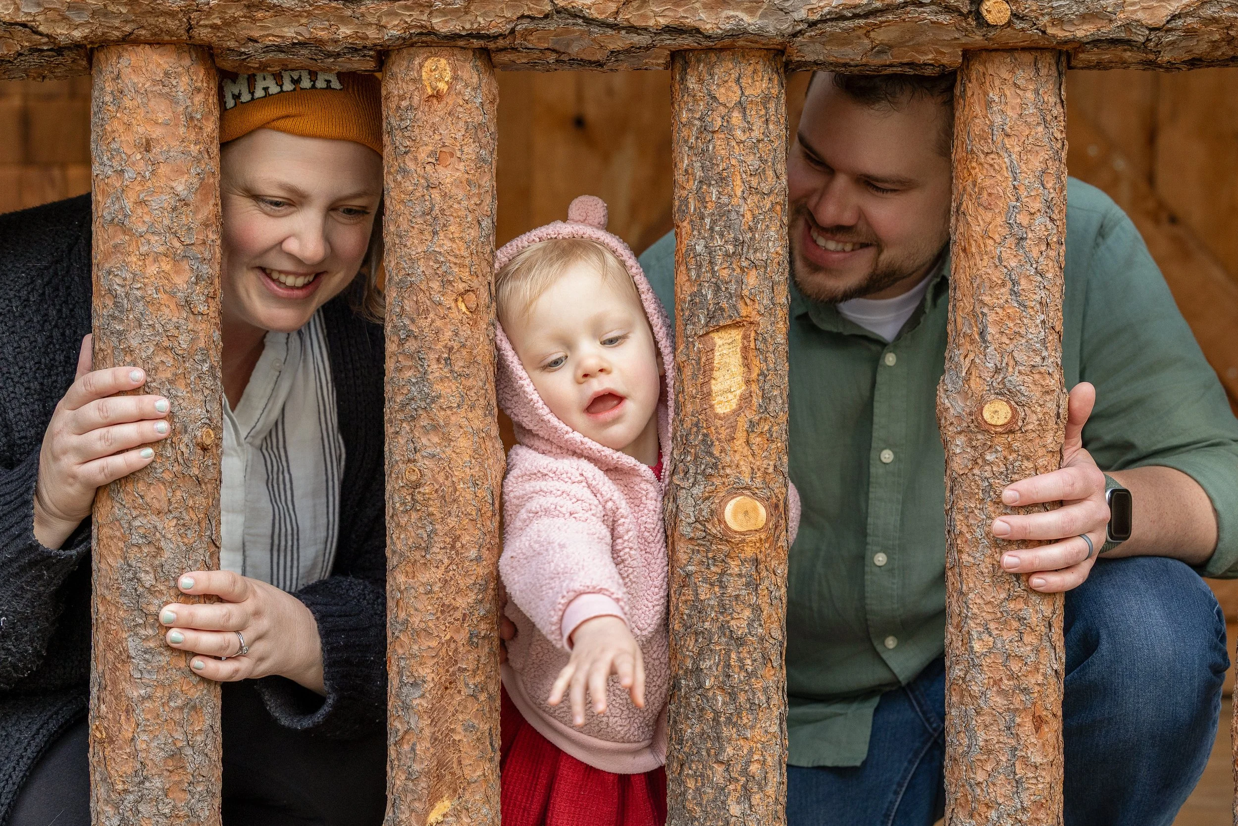 Adam and Jessie laugh as their daughter stretches between the log railings at Camp Richardson, reaching for something just out of frame. Documentary family portrait by Ruwan & Diana Photography.