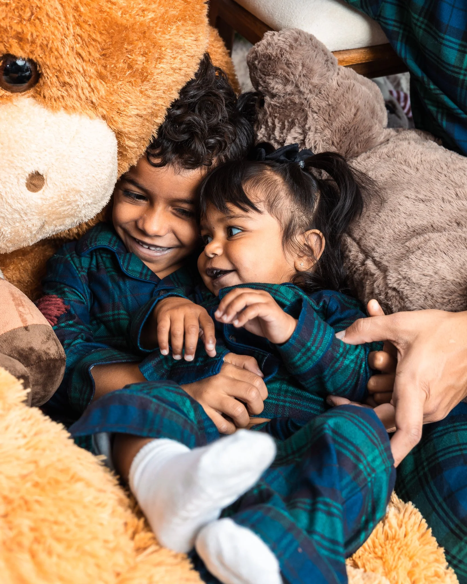 Two siblings laughing together surrounded by stuffed animals in pajamas, documentary family photography San Diego