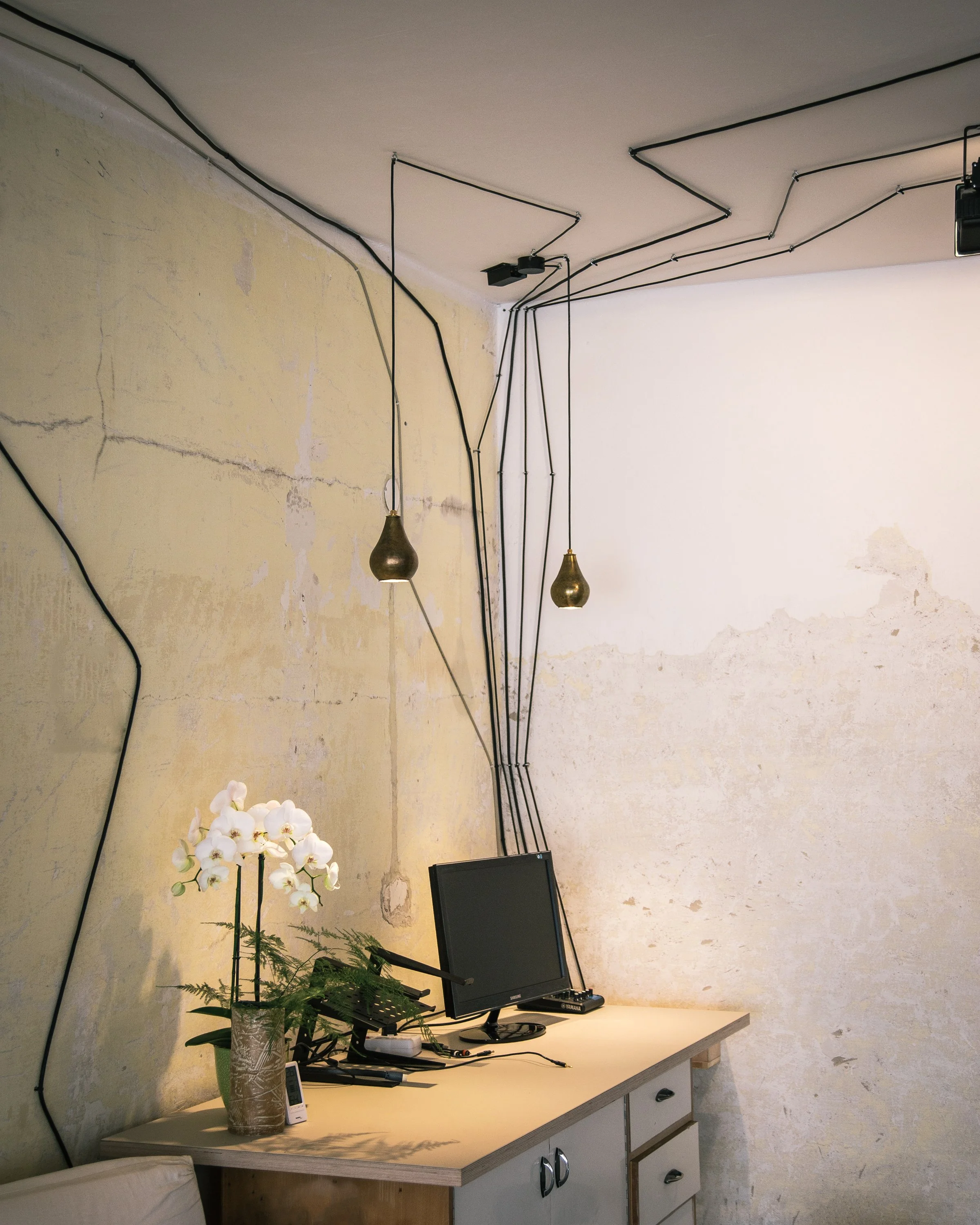 Technikpult im Veranstaltungsraum mit Laptop, Audio Mischer, Pflanze und goldenen Lampen über dem Pult.