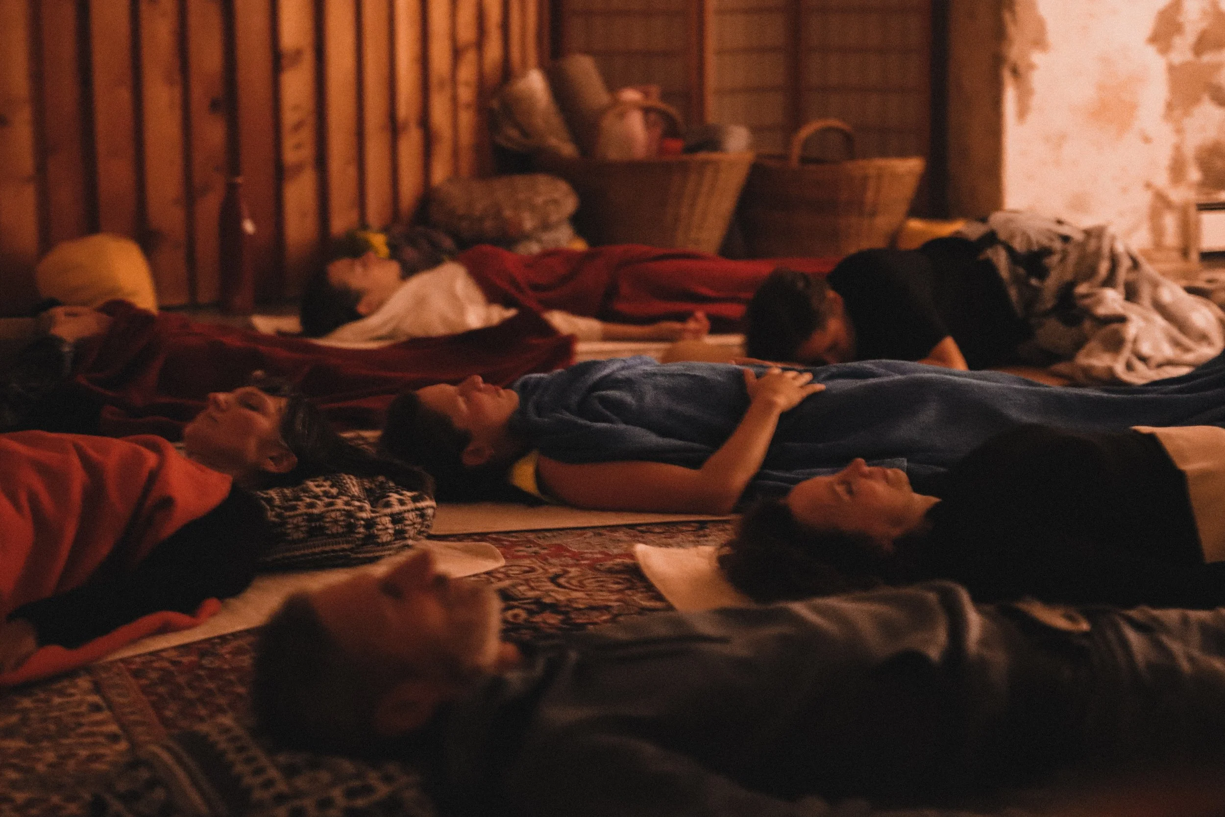 Mehrere Personen liegen auf Teppichen und Matten in einem warm beleuchteten Raum, für eine Meditation und Entspannung nach einem Liberation Dance.