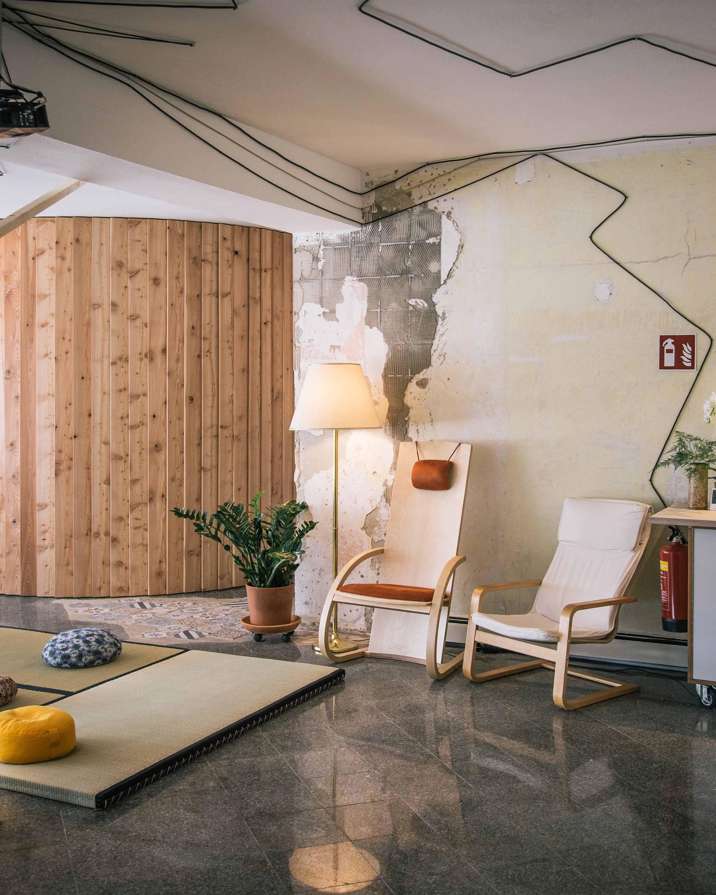 Gemütlicher Veranstaltungsraum mit zwei Sesseln, Tatami Matten, mehreren Sitzkissen, einer Stehlampe und einer Pflanze.