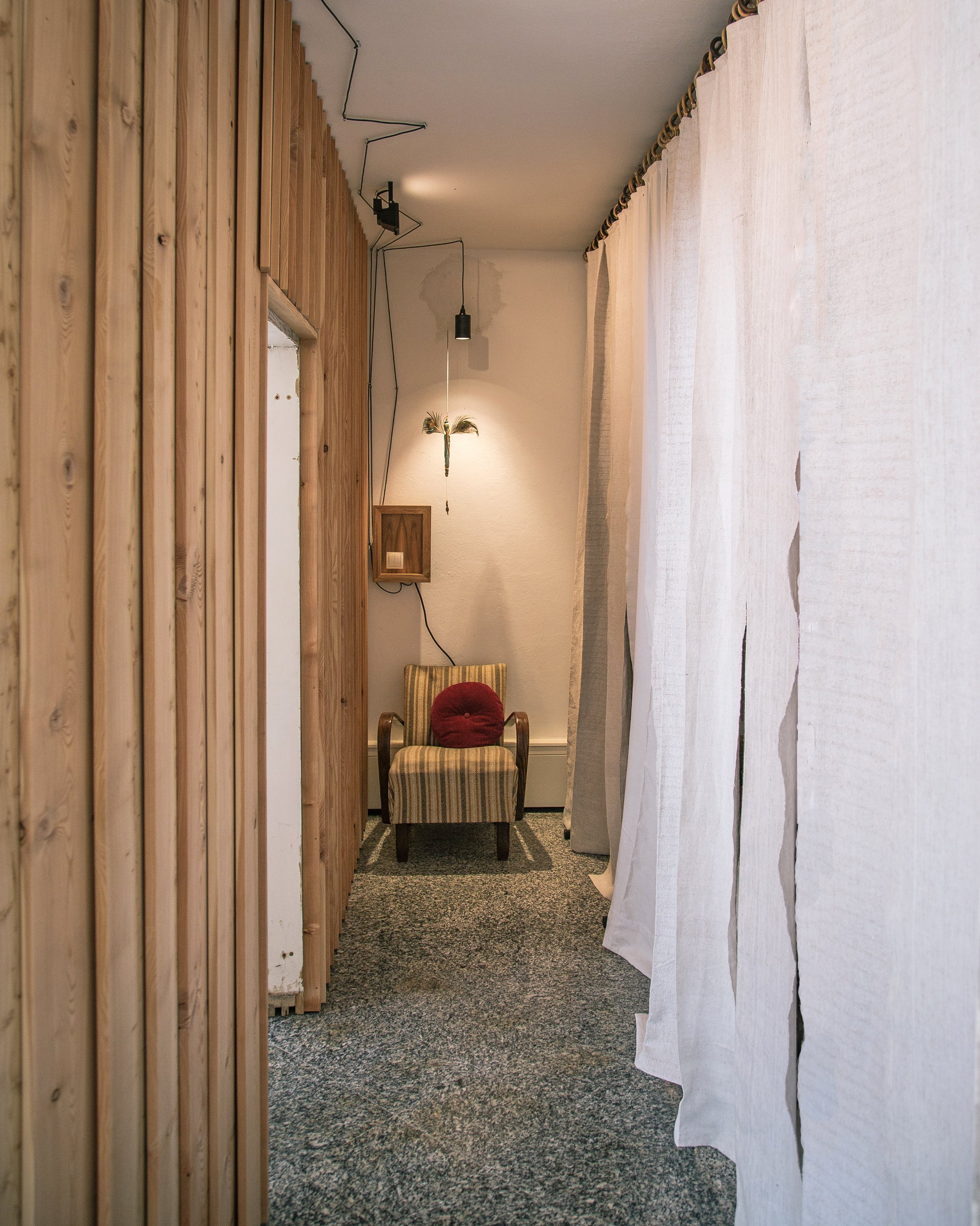 Ein schmaler Durchgang, dekoriert mit einem Armlehnenstuhl, einer roten Kissen. Ganz hinten ist ein Gemälde an der Wand.