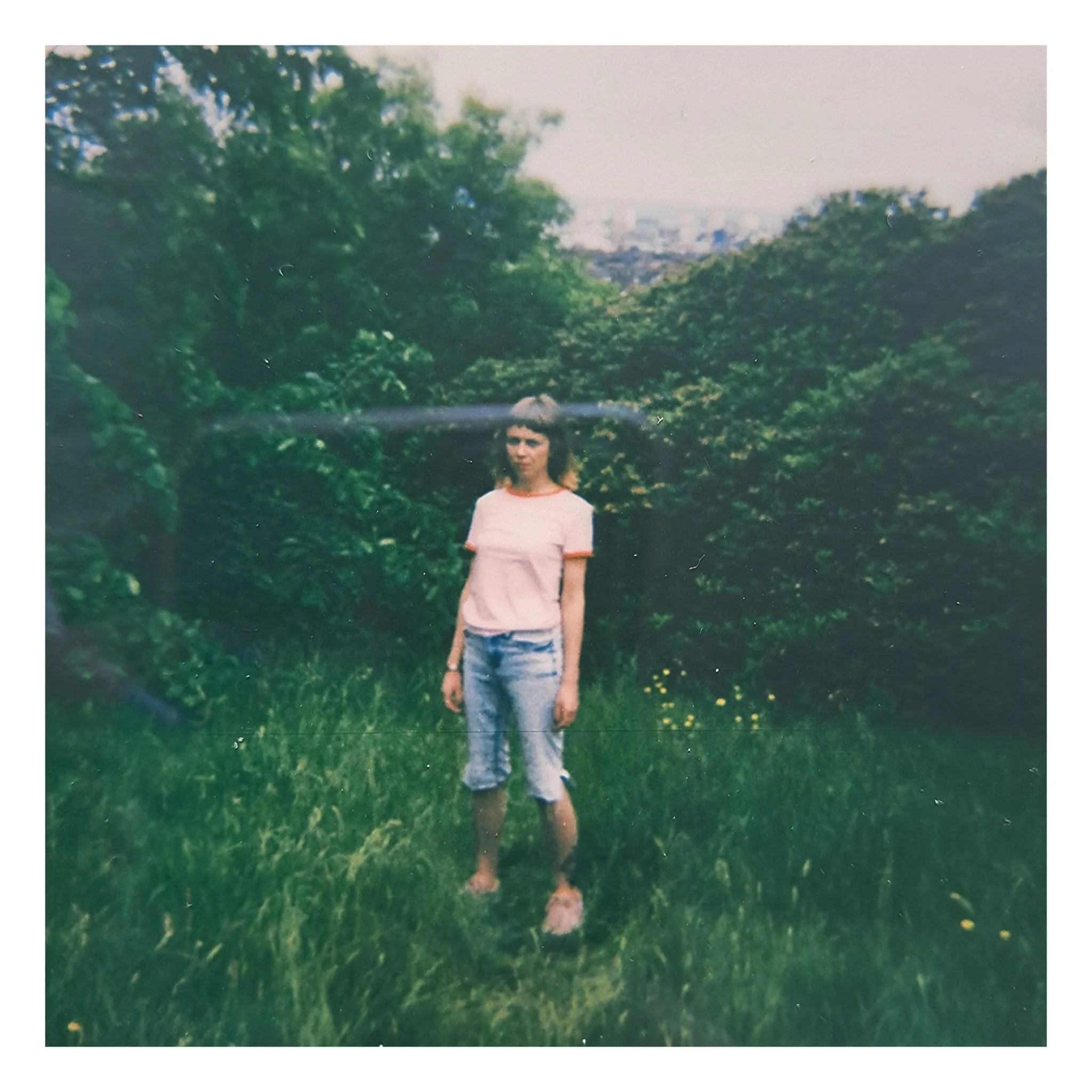 Carla J Easton Album artwork - I Think That I Might Love You.  A woman standing barefoot on grass in a lush green garden or park, with trees and bushes in the background, during daytime.