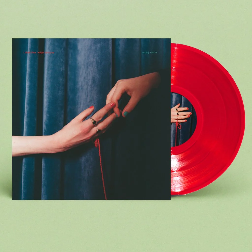 A red vinyl record partially overlays the album cover for Carla j. Easton's "I think that I might love you," which features two hands reaching toward each other against a blue curtain background. The album cover has small red text in the top left and top right corners.