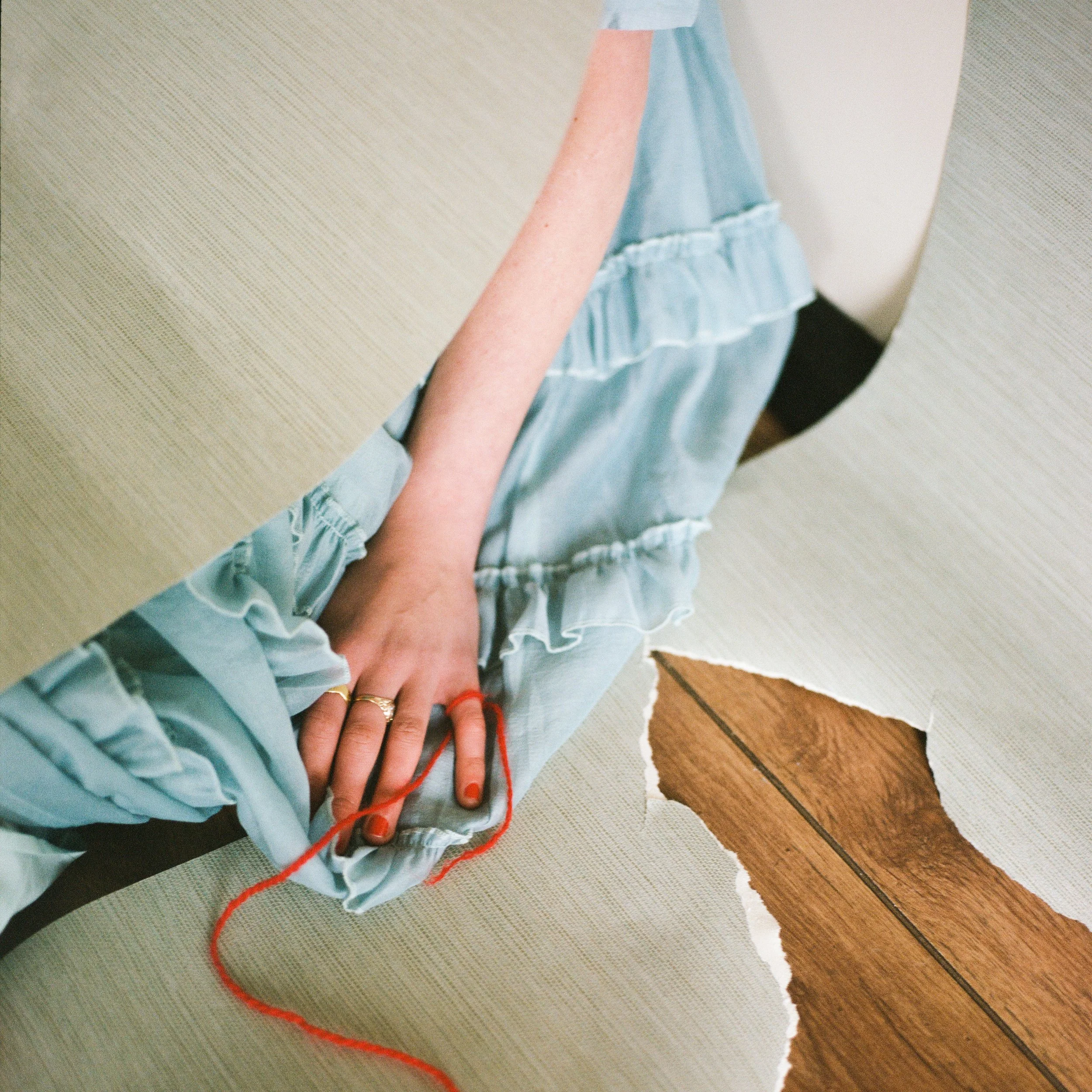 Carla J Easton Album artwork - I Think That I Might Love You A person wearing a light blue dress with ruffles is sitting on a black chair, with a torn piece of wallpaper on wooden flooring nearby.