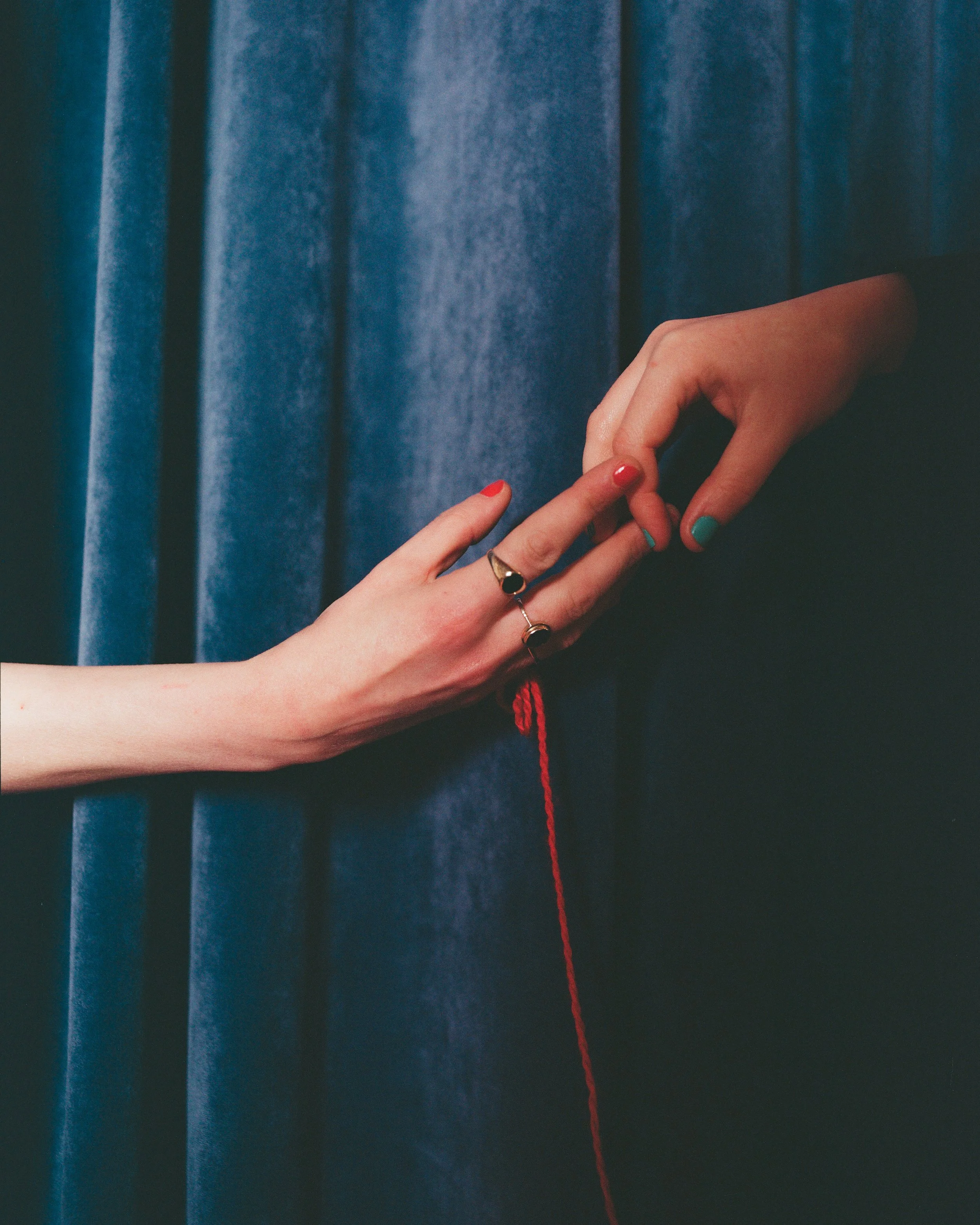 Carla J Easton Album artwork - I Think That I Might Love You. Two hands reaching out, one with painted nails and rings, green and red, holding a red thread in front of a blue curtain.