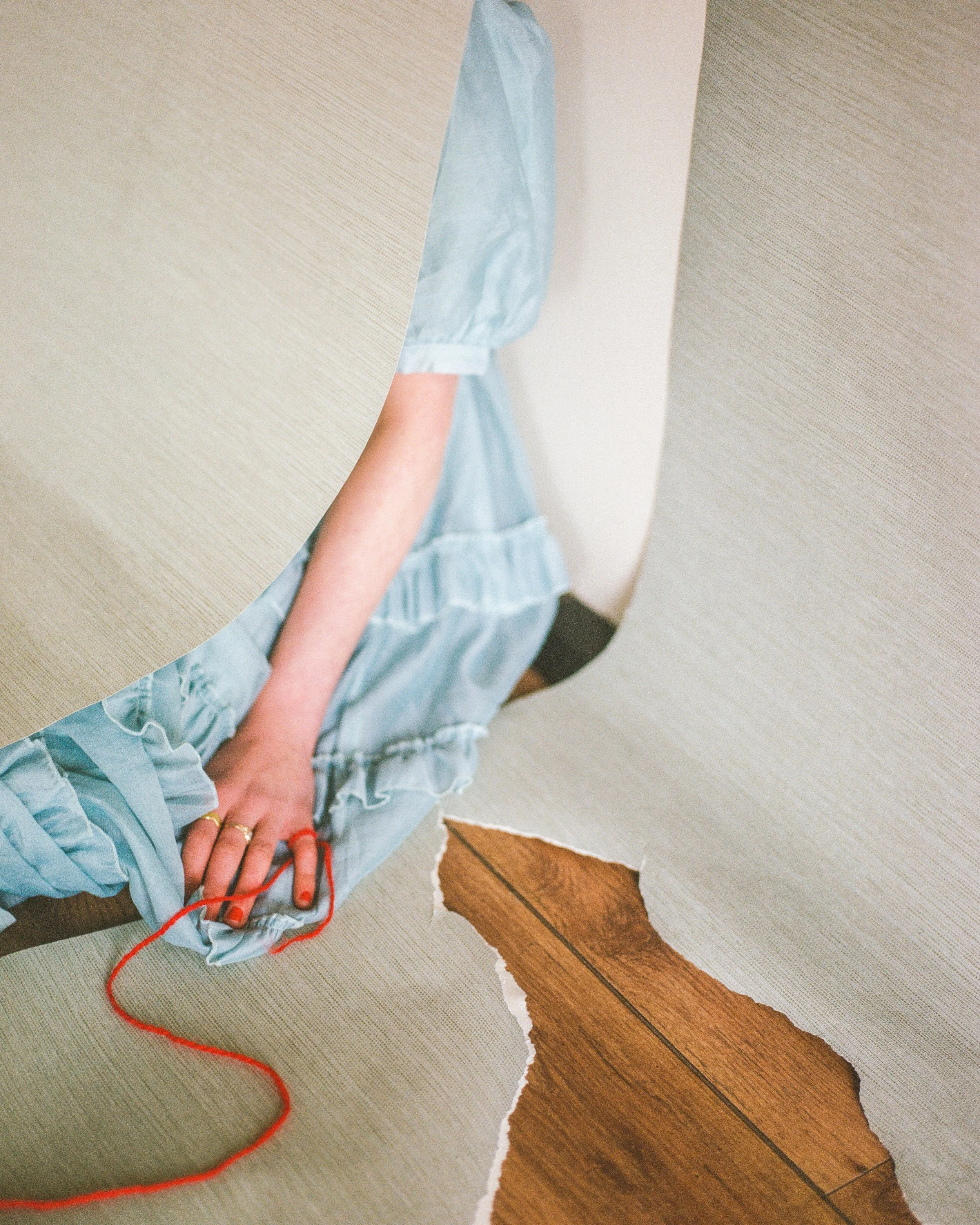 Carla J Easton Album artwork - I Think That I Might Love You Person sewing with red thread on a light blue dress, reflected in a mirror, with torn wallpaper on wooden floor.