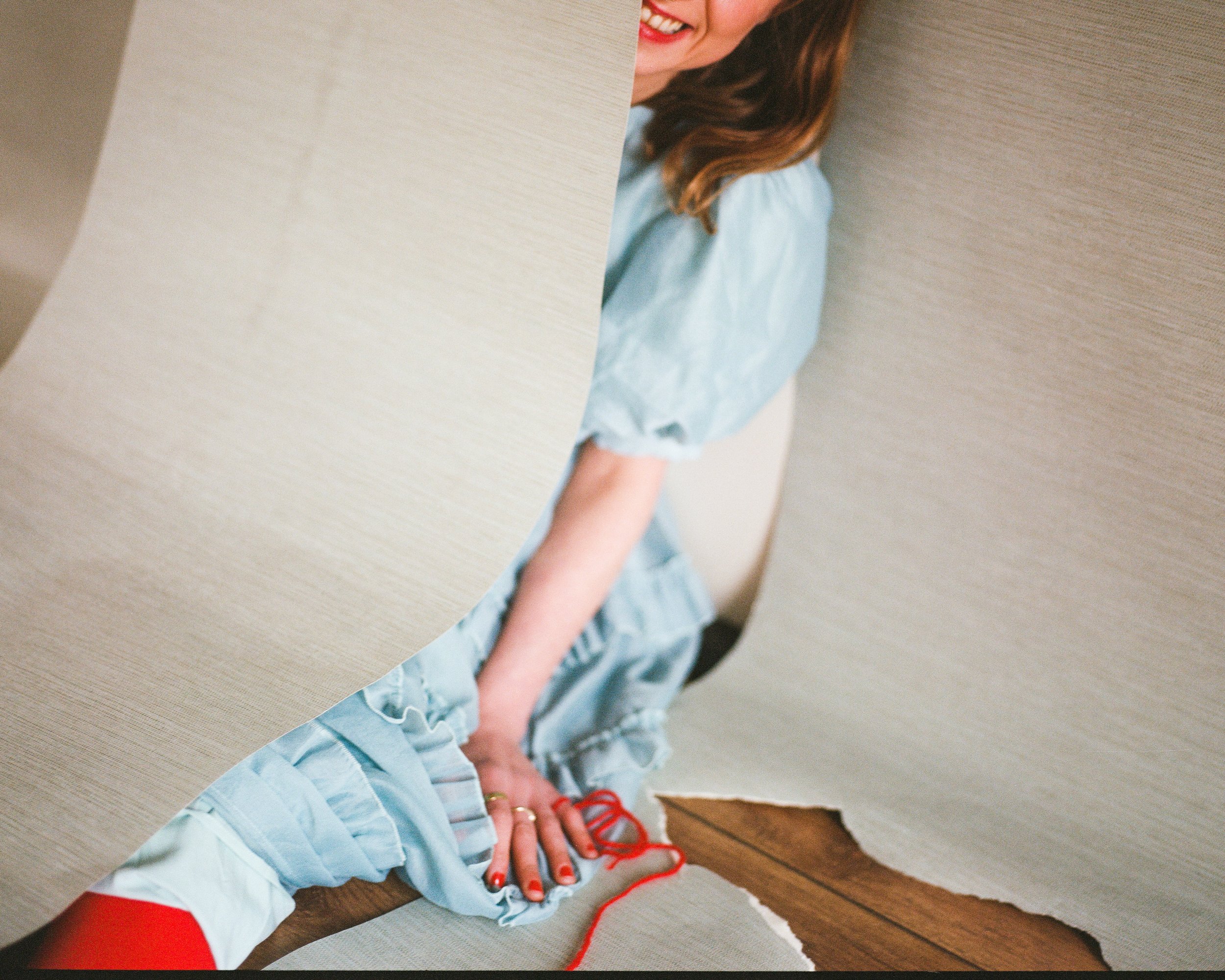 Carla J Easton Album artwork - I Think That I Might Love You  A person in a blue dress with red nail polish is seen through a torn hole in a wall or paper, smiling with their face partially visible.