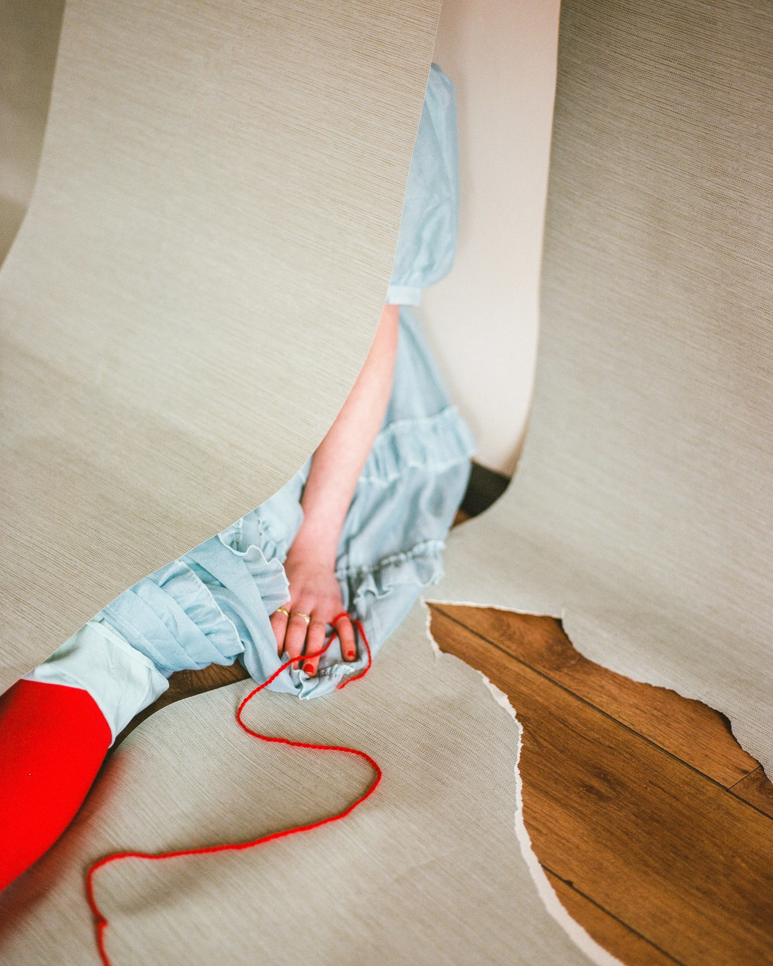 Person tearing up a beige wallpaper to reveal wood flooring beneath.
