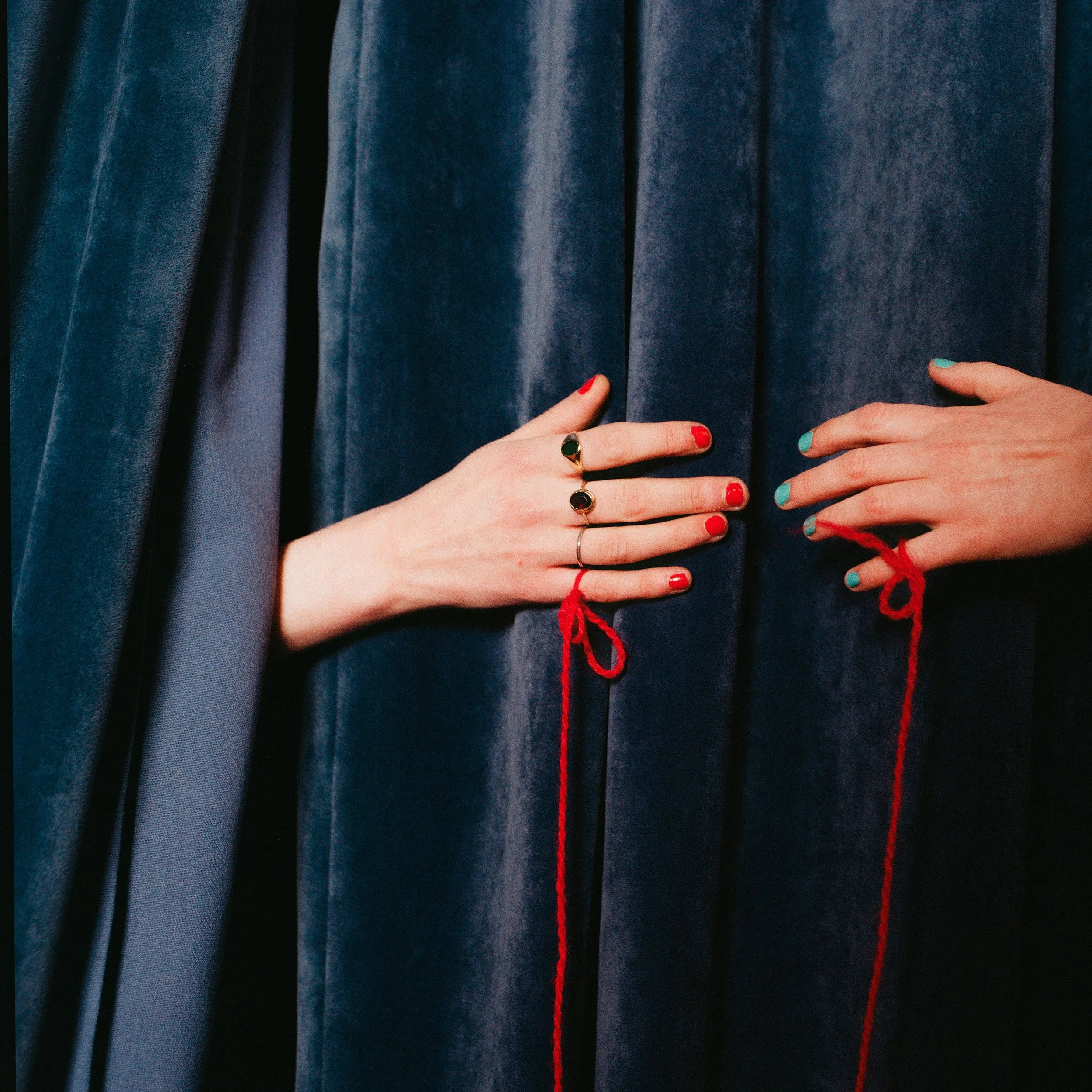 Carla J Easton Album artwork - I Think That I Might Love You Close-up of two hands with colorful nails and rings, holding red yarn against dark blue velvet curtains.