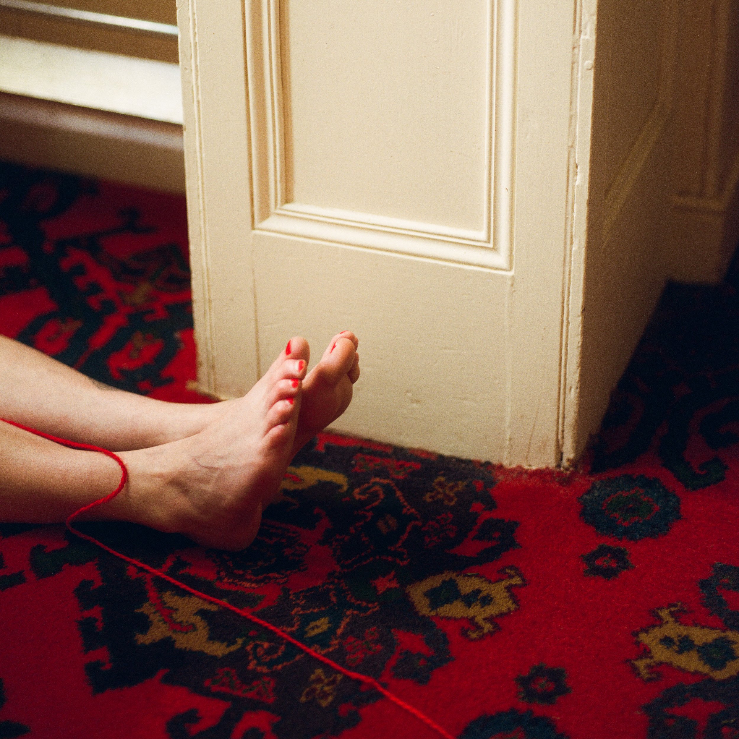 Carla J Easton Album artwork - I Think That I Might Love You A woman sitting on a red and black patterned carpet with her legs extended and her toes painted red, near a cream-colored door with a decorative panel.