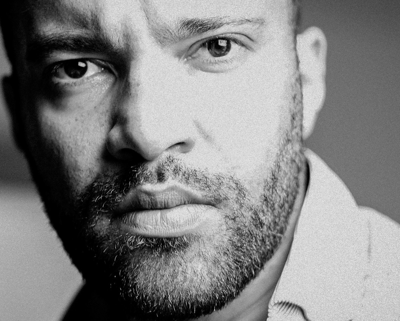 Nahaufnahme eines Mannes mit Bart und nachdenklichem Blick, schwarz-weiß.