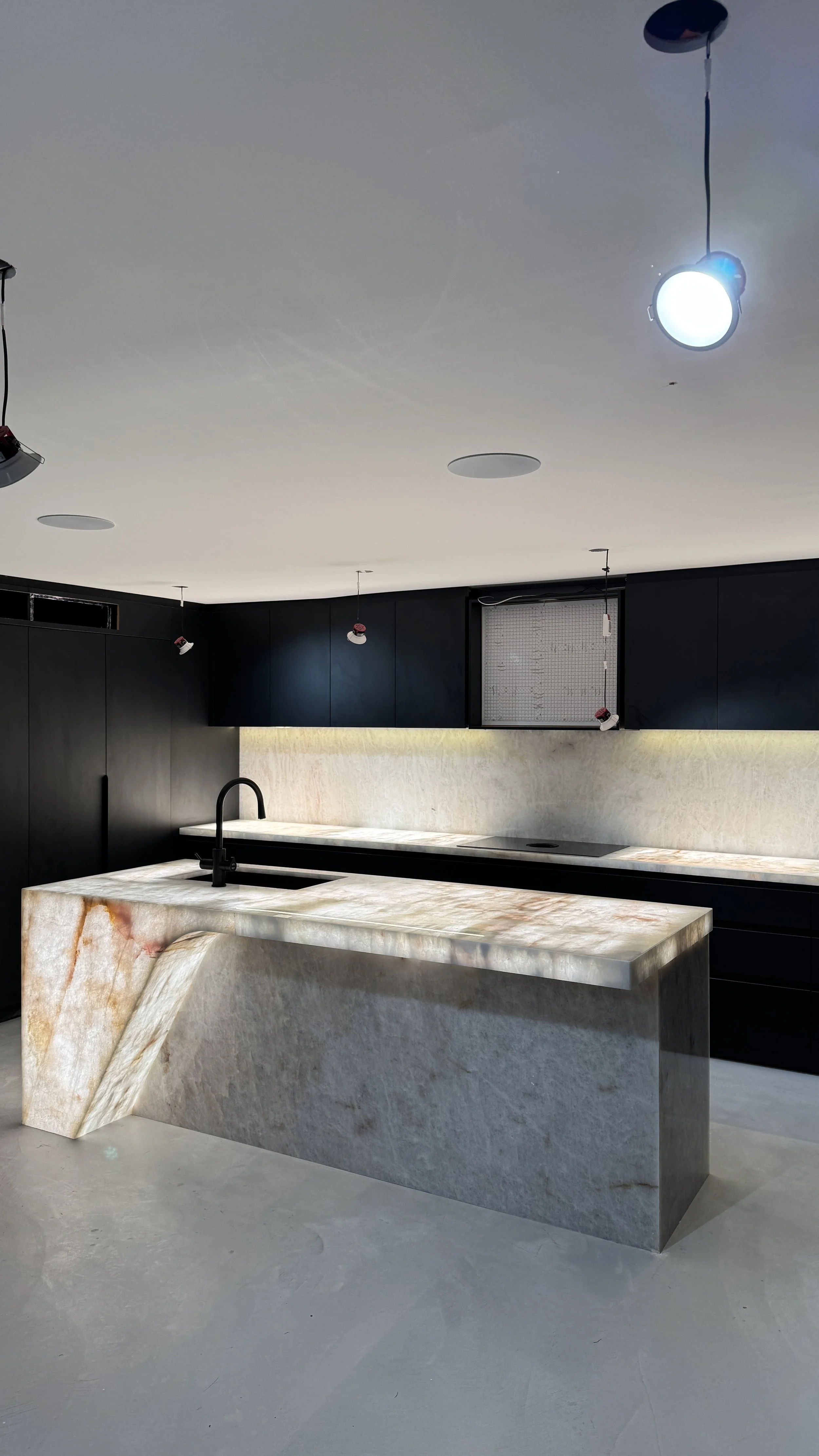 Modern kitchen with a large marble island, black cabinetry, and a black faucet.