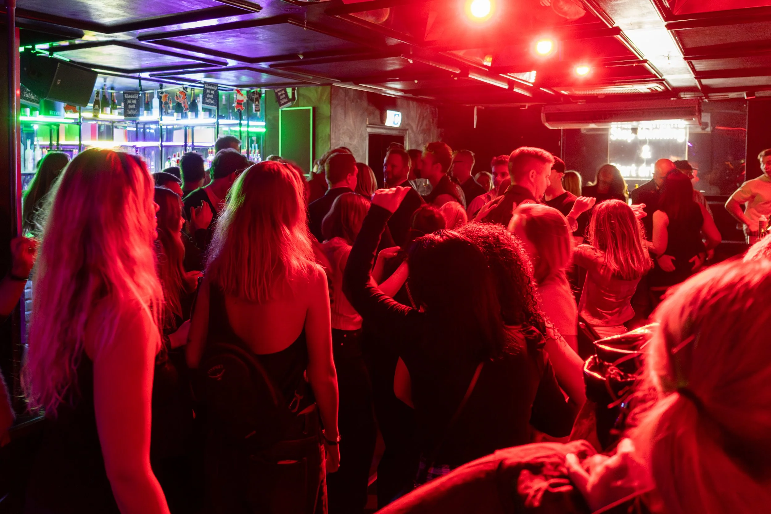 People dancing and socializing in a nightclub with red and neon lighting.