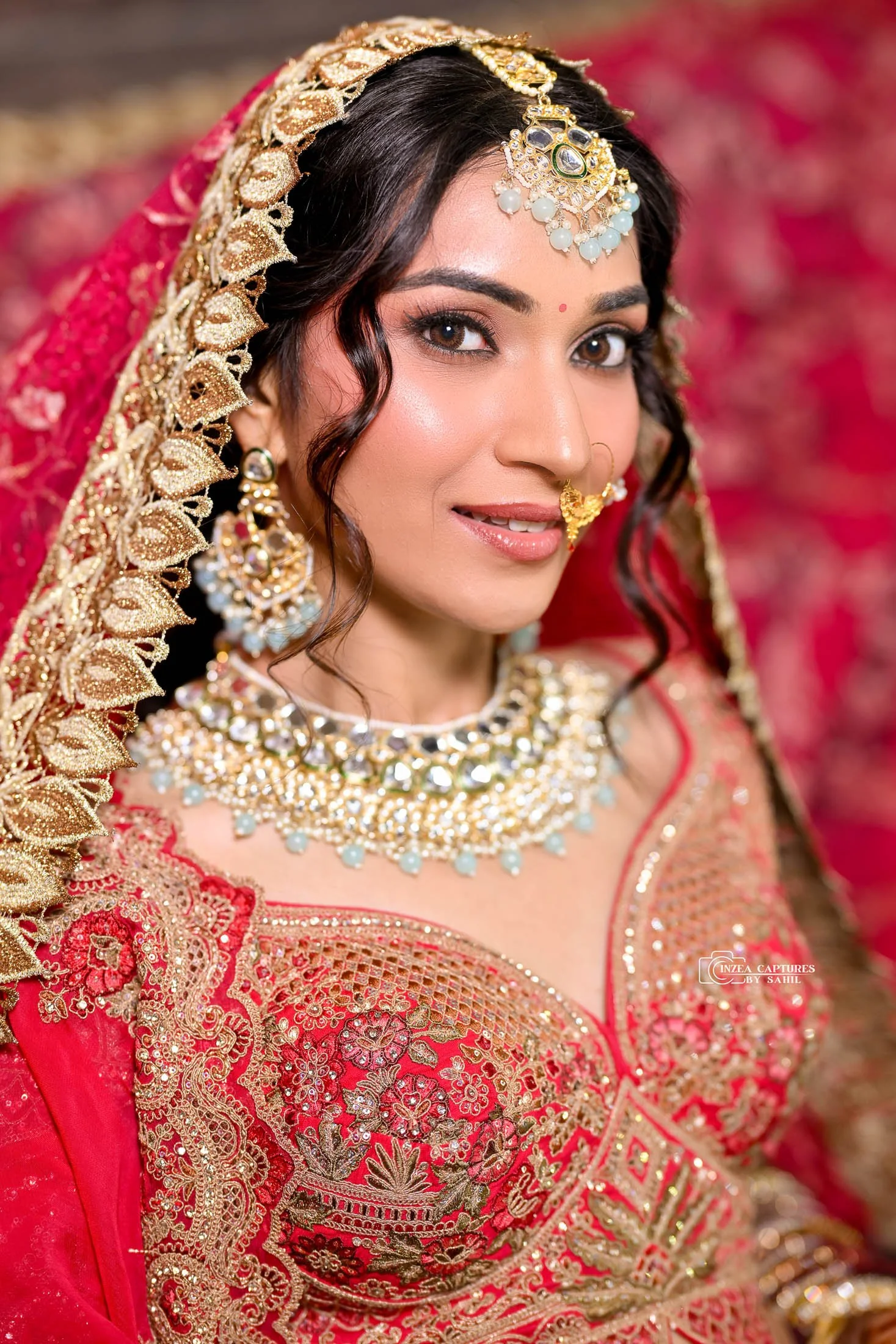 A woman dressed in traditional Indian bridal attire with intricate gold jewelry and a red and gold embroidered saree.