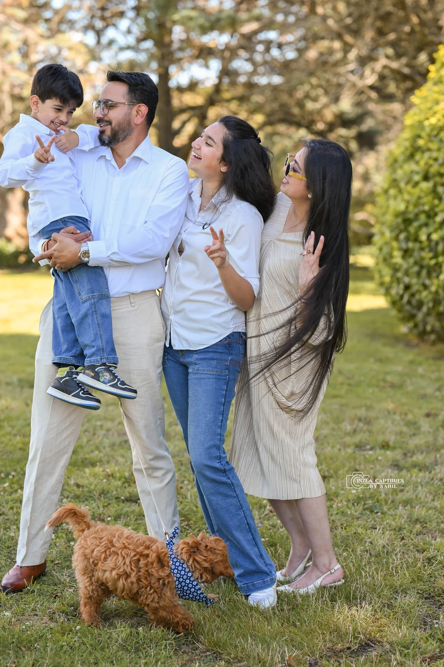A happy family of four and a small dog outdoors in a park, smiling and enjoying time together.