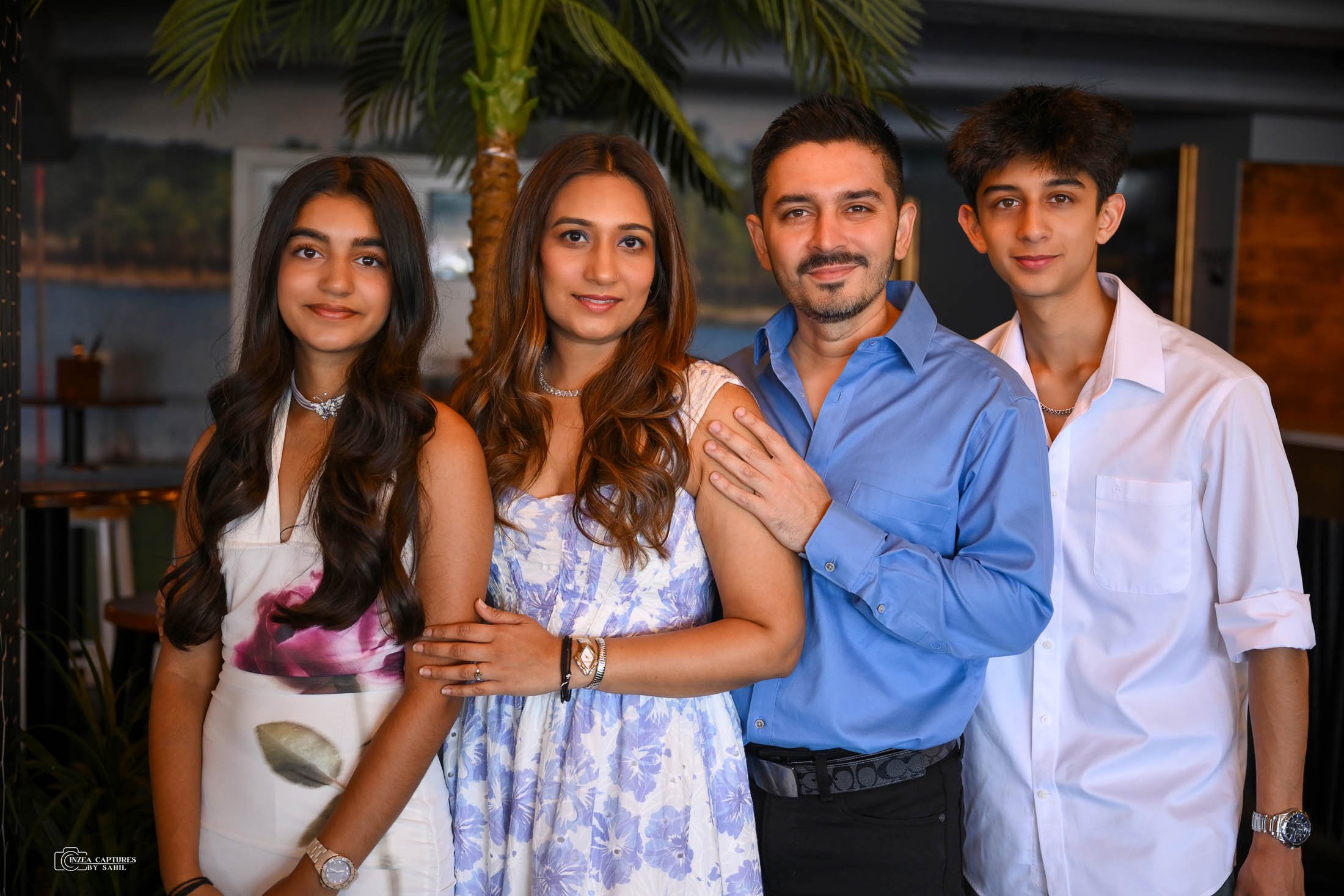 Family of four posing together indoors, with a palm tree in the background.