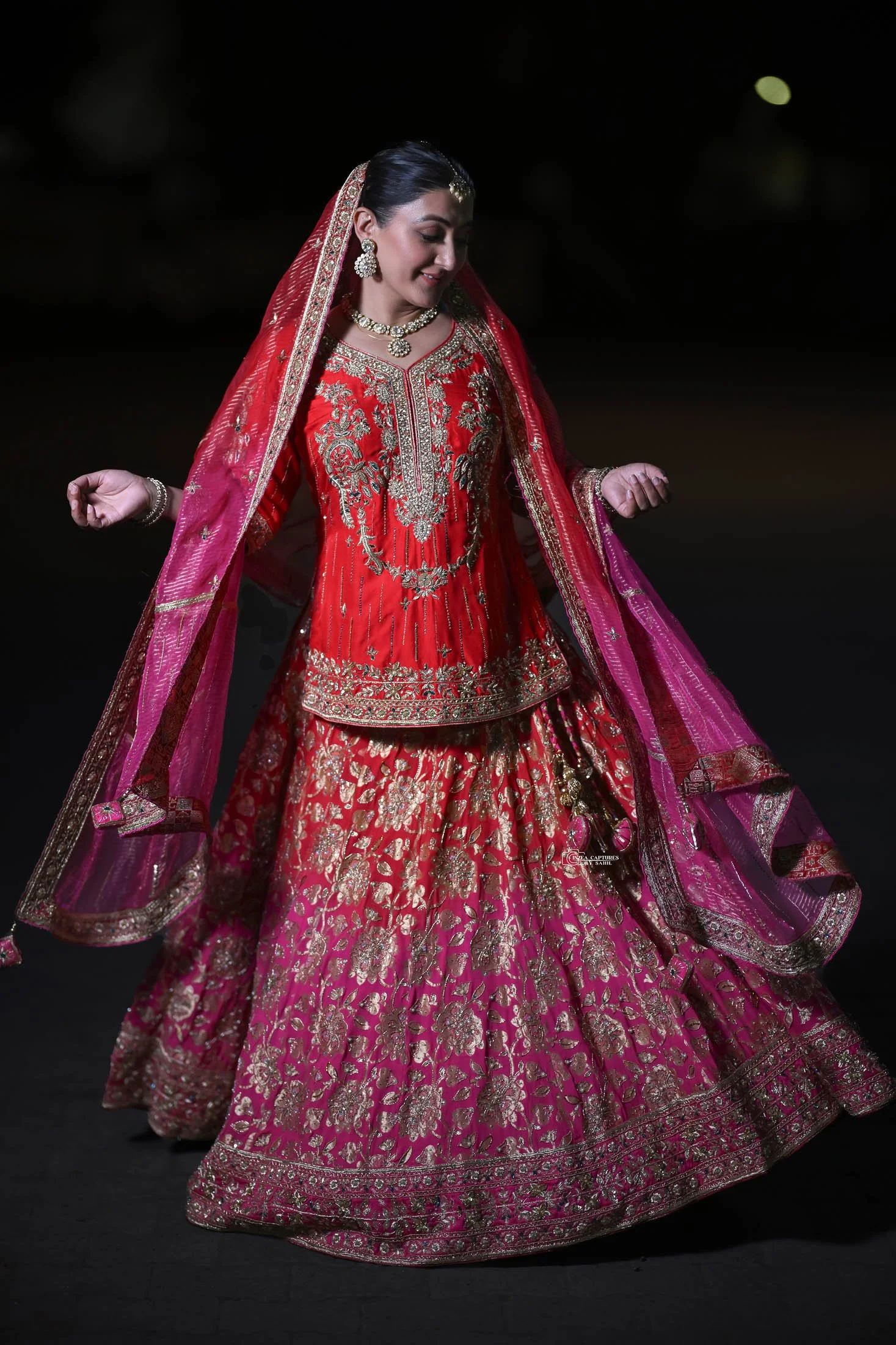 Woman in traditional Indian bridal attire dancing in dark background.