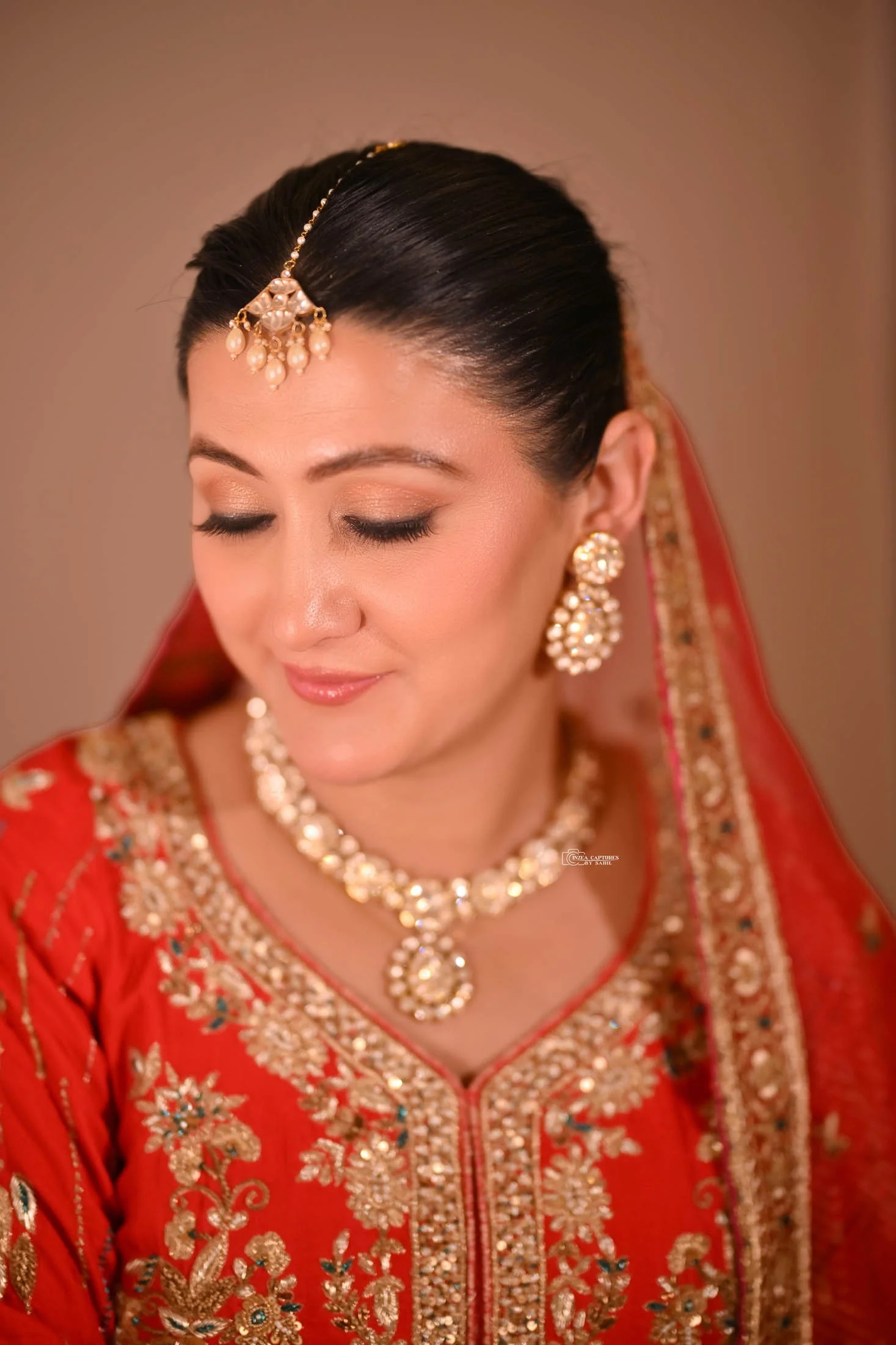 A woman dressed in traditional Indian attire with intricate jewelry, including earrings, necklace, and a headpiece, with eyes closed and a serene expression.