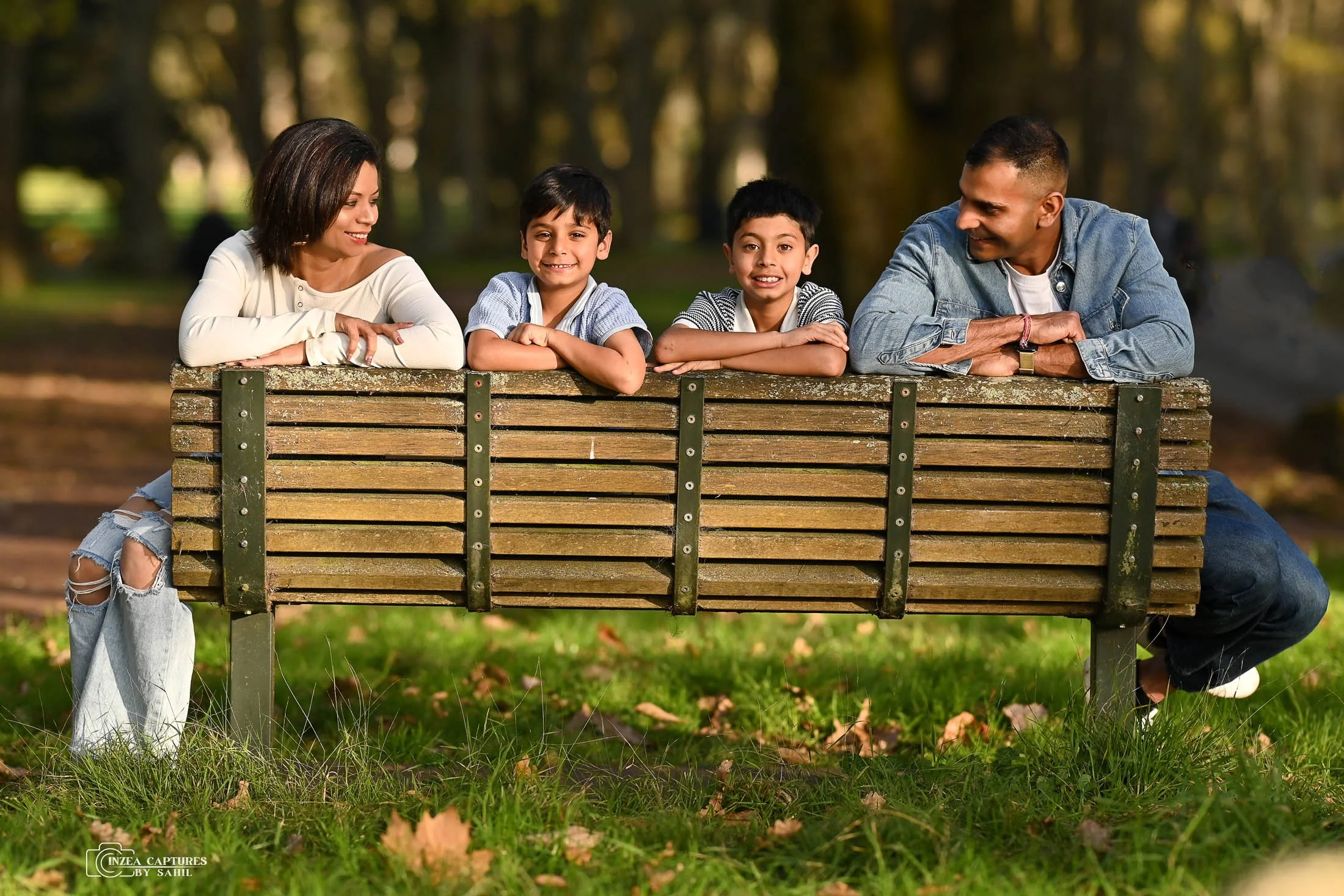 A family of five sitting on a park bench, smiling and enjoying their time together in a wooded outdoor setting.