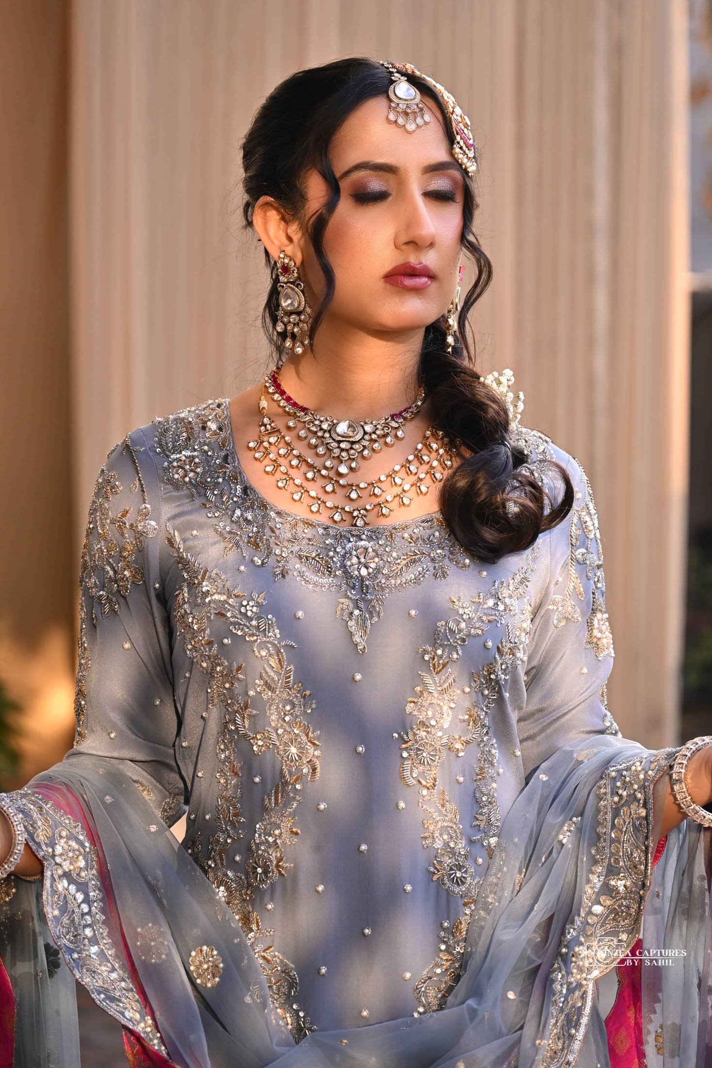 A woman in traditional South Asian attire with elaborate jewelry, closed eyes, and a serene expression.