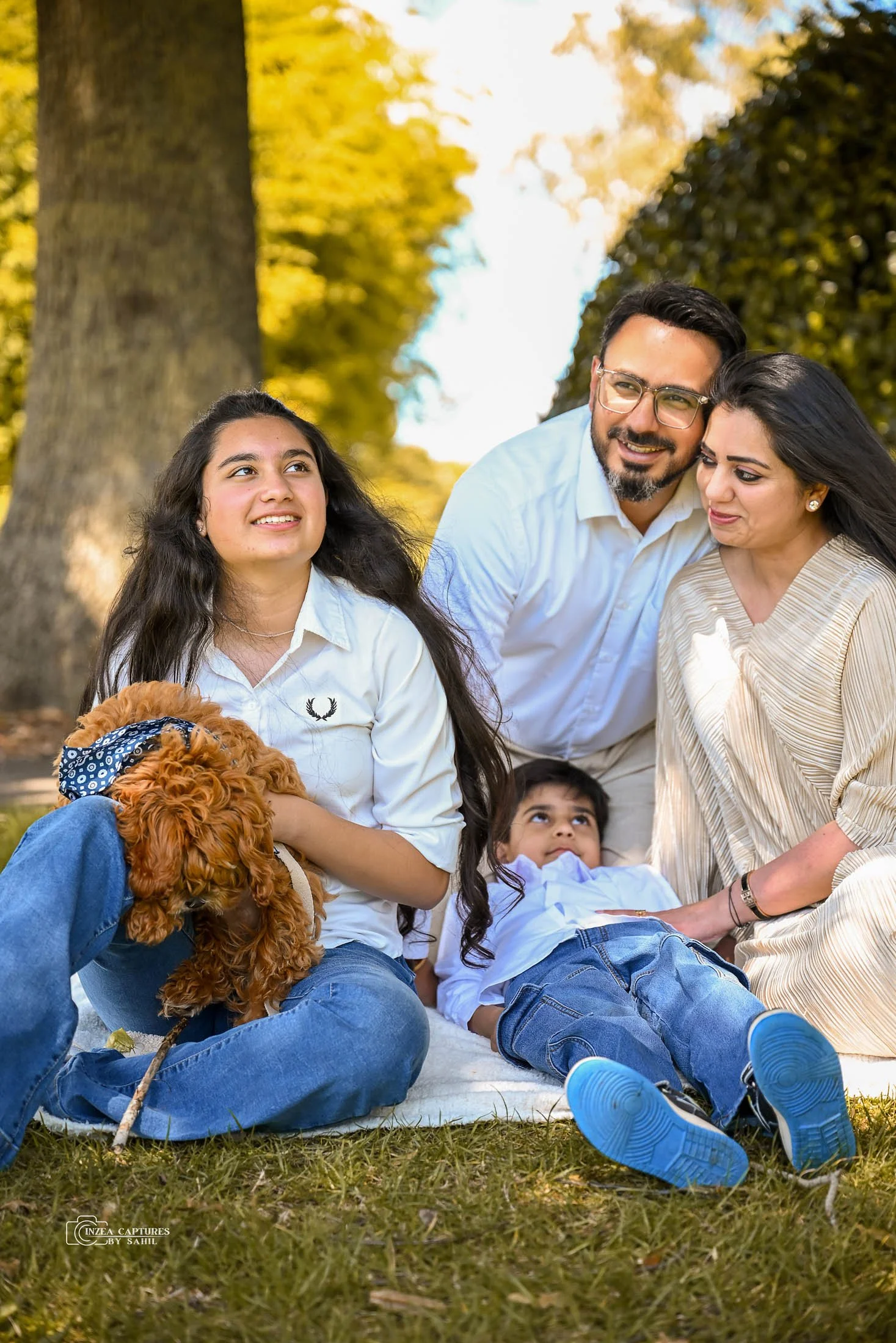Family of four with two children and a dog having an outdoor picnic in the park during autumn.