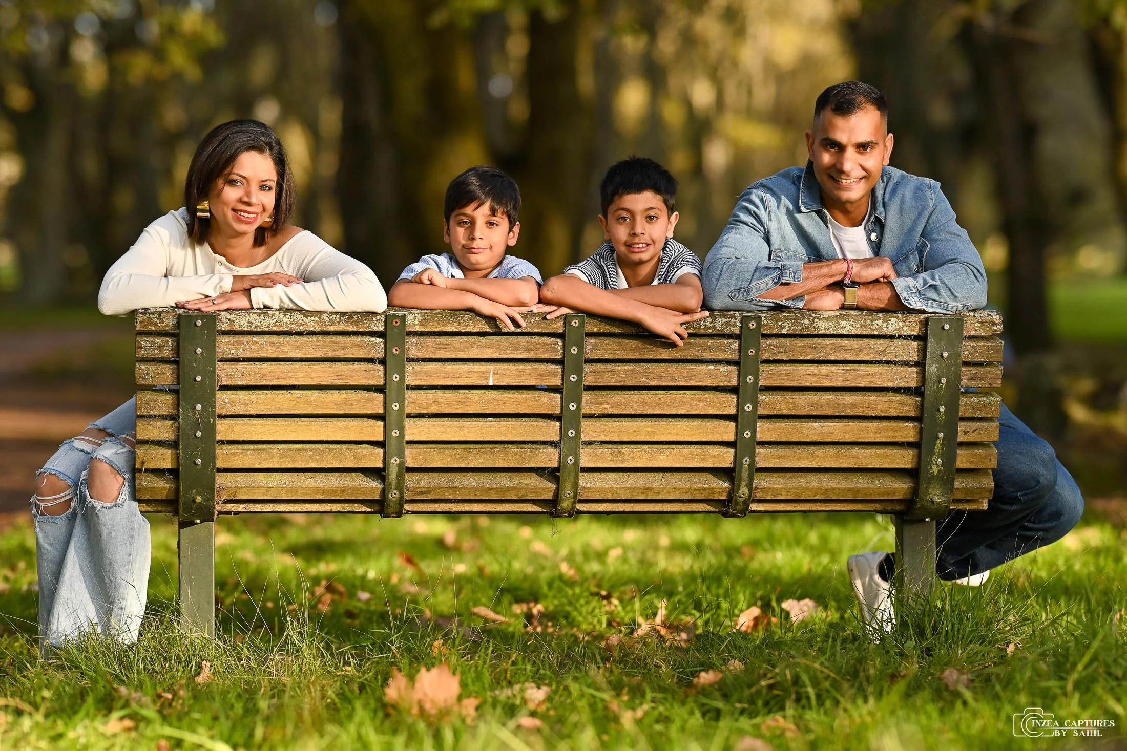 A family of five leaning on a park bench in a forested area, smiling and enjoying the outdoors.