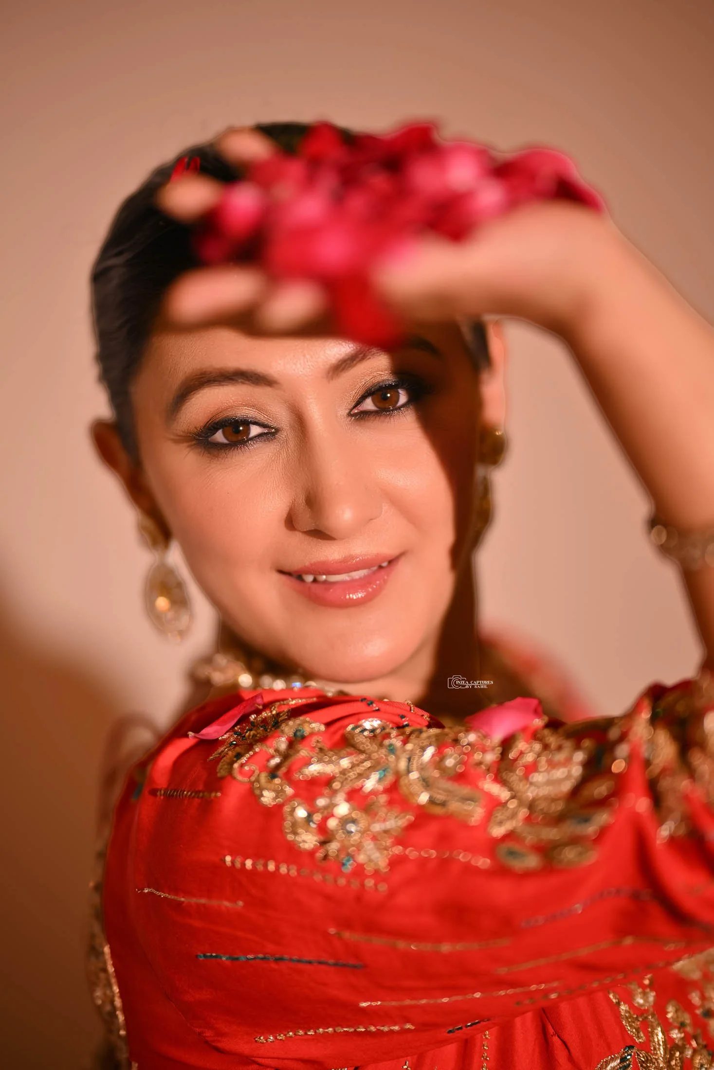 A woman in traditional attire smiling and holding pink flower petals above her head.
