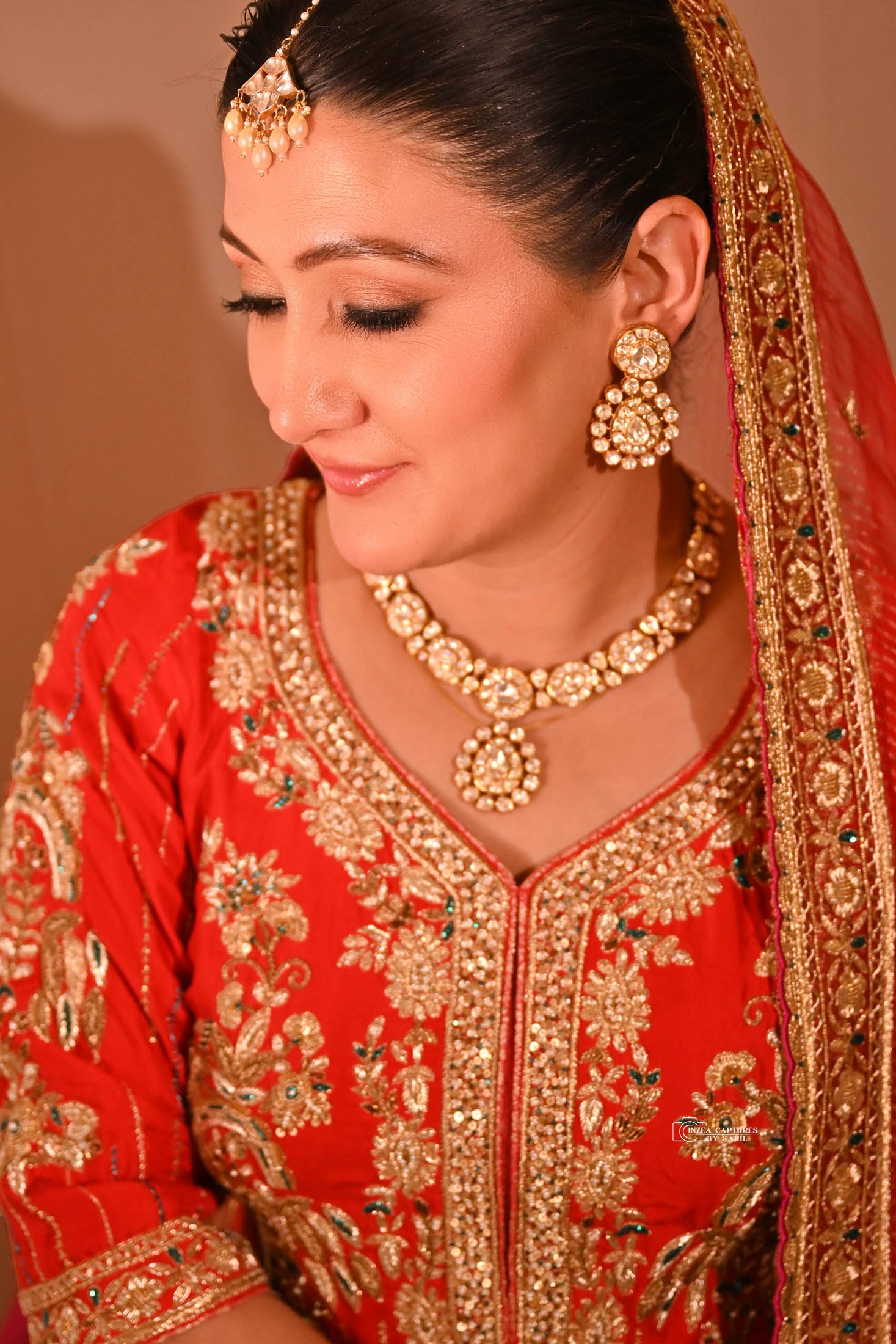 Woman wearing traditional Indian attire with red embroidered dress, gold jewelry including necklace, earrings, and headpiece, and a red and gold dupatta.