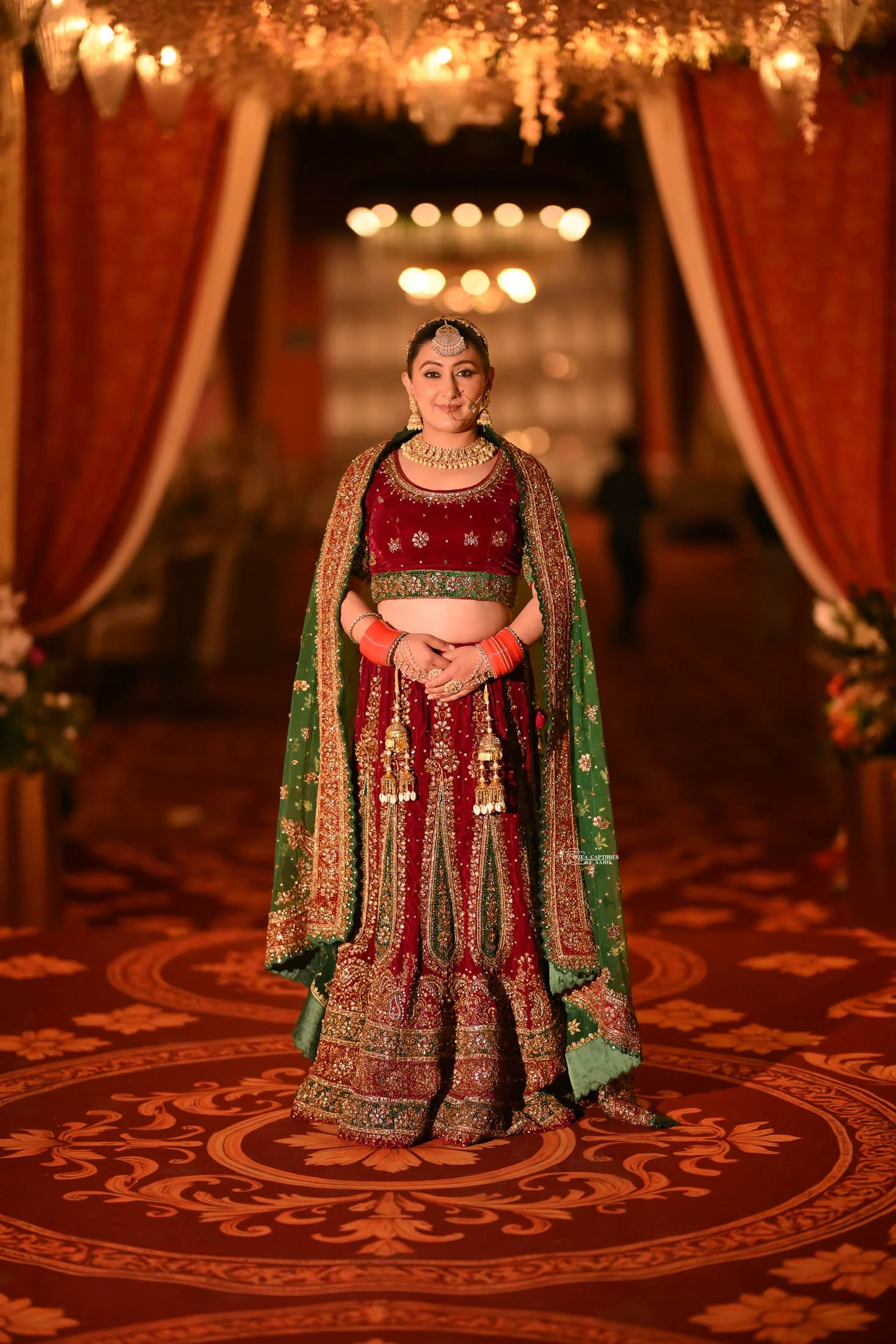 A woman dressed in traditional Indian bridal attire standing in a decorated wedding hall.