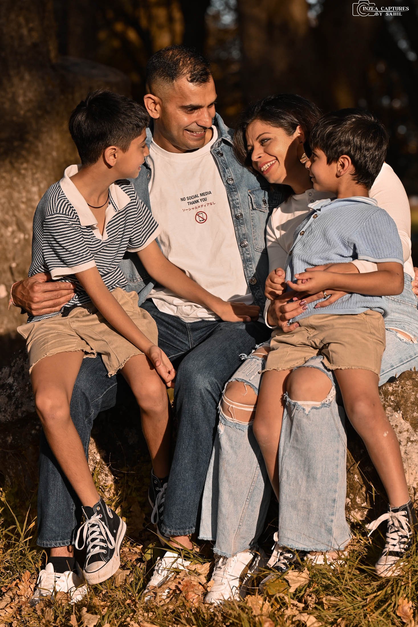 A family of four sitting on a large rock outdoors, smiling and hugging each other during the daytime.