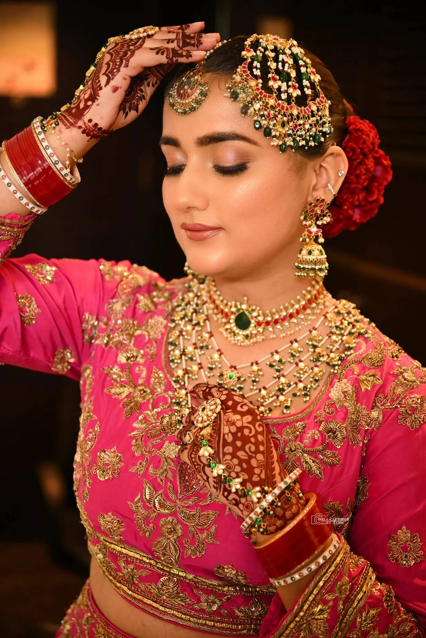 A woman dressed in traditional Indian bridal attire, wearing a pink saree with gold embroidery, ornate jewelry, and mehndi on her hands, with her eyes closed and a serene expression.