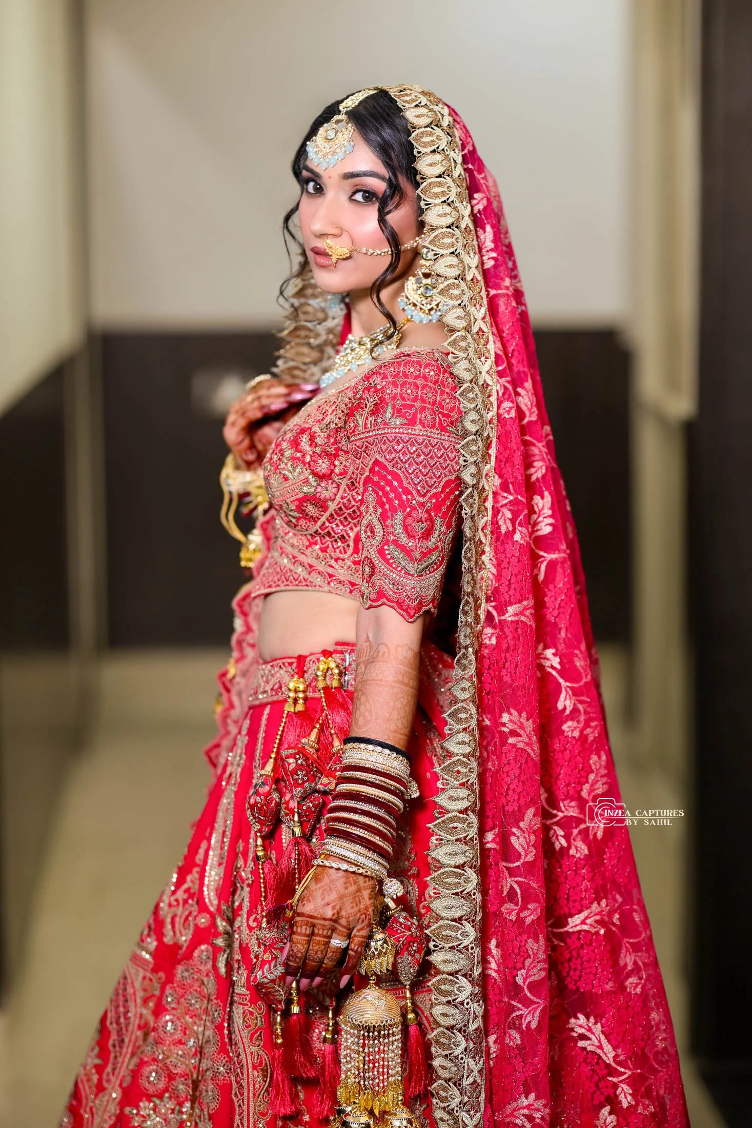 A woman dressed in traditional Indian bridal attire, wearing a red embroidered saree with gold jewelry and henna on her hands.
